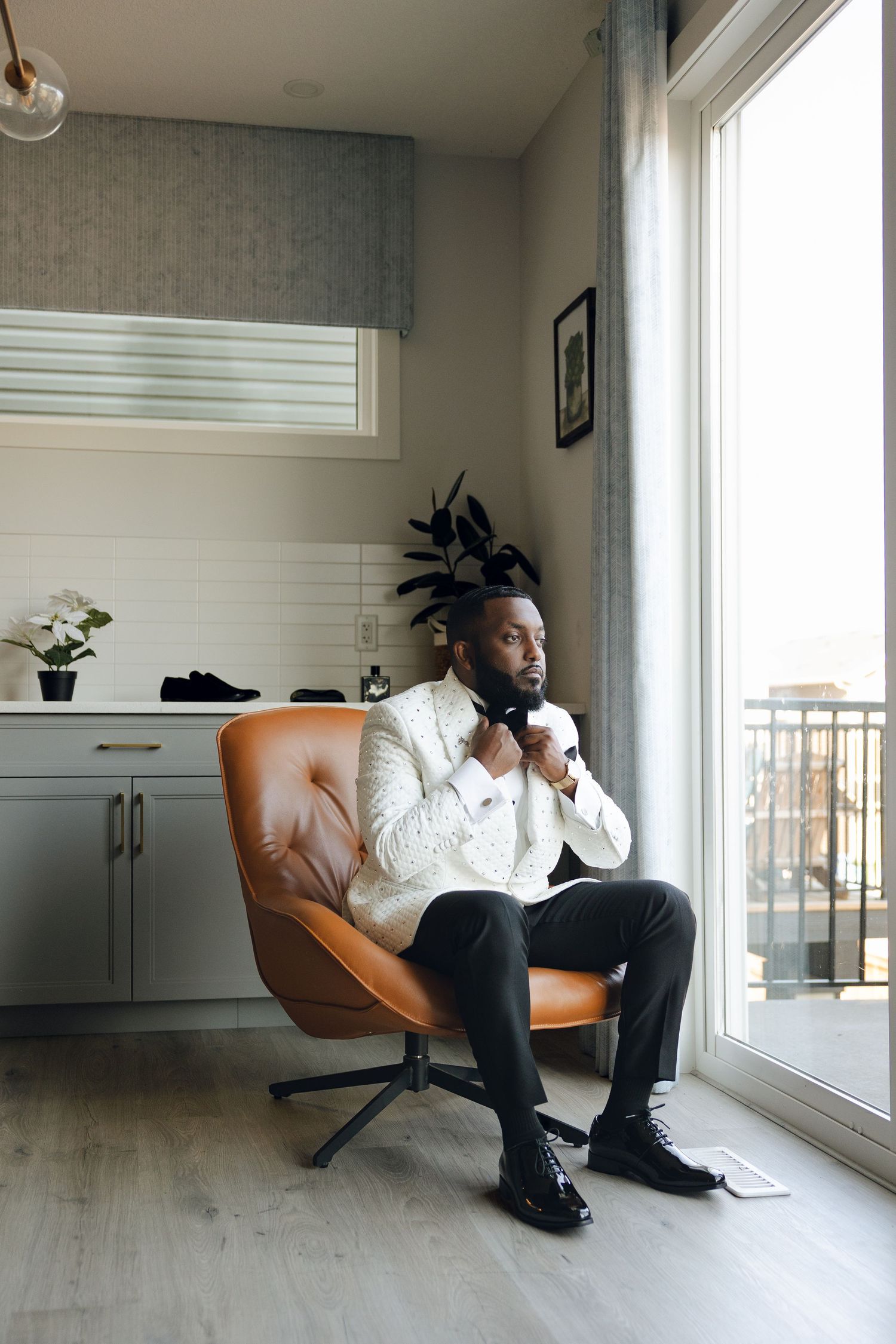 A modern orange chair is positioned against a white wall in a minimalist room with grey floors and large windows.