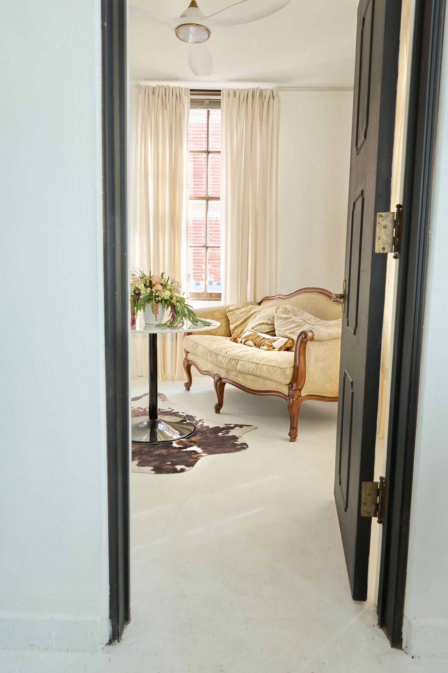 Bright bedroom with white walls, hardwood floors, and a classic wooden bed frame near large windows.