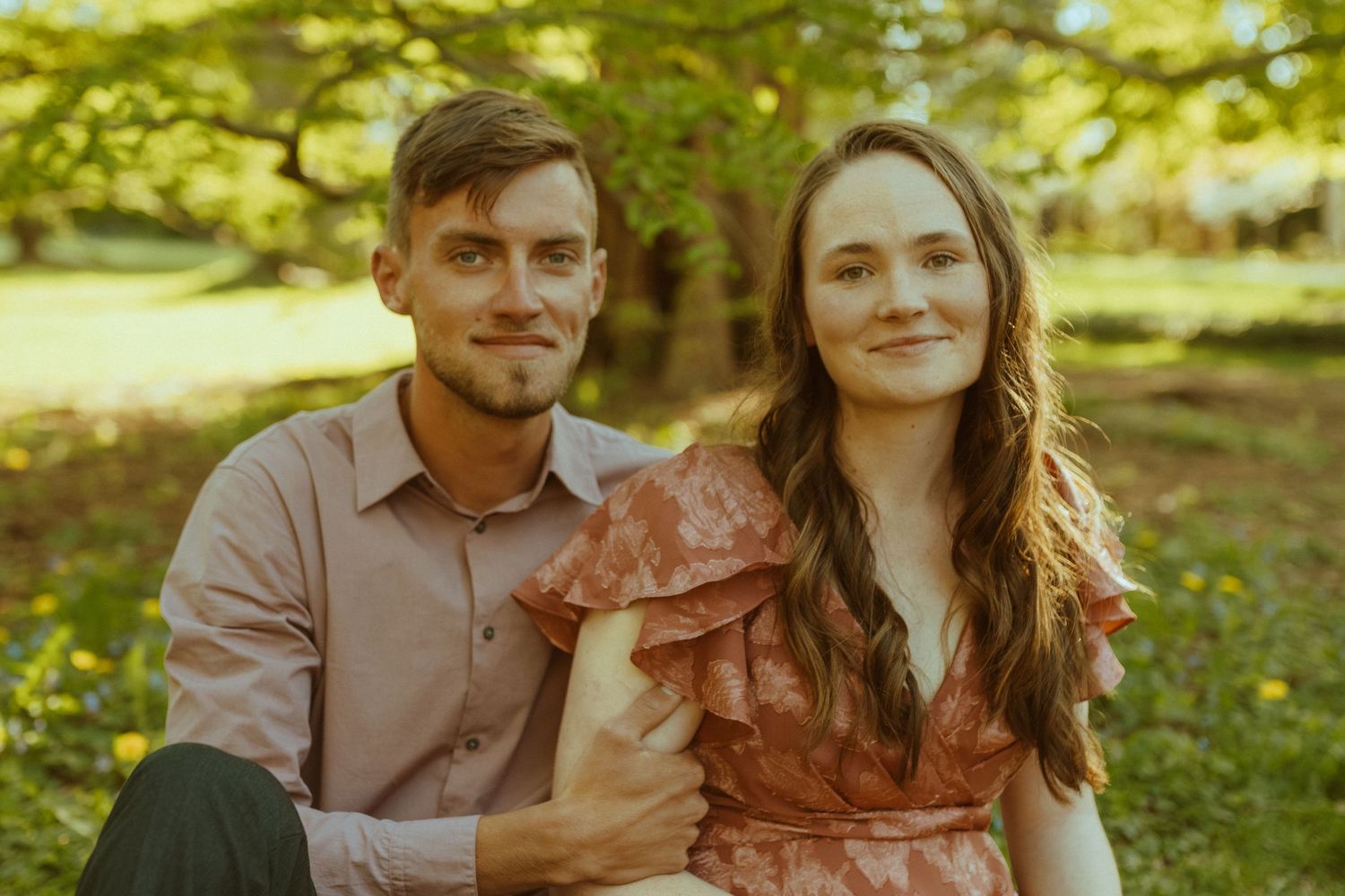 Romantic couple in casual attire enjoying intimate moments in a sunlit garden setting.