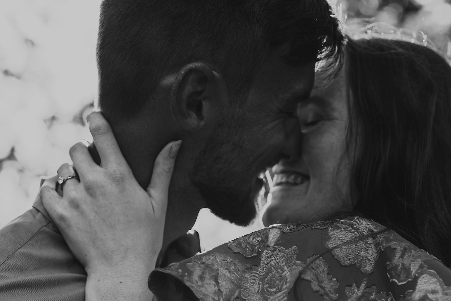 Two people share a tender kiss while sitting together in an intimate black and white photograph.