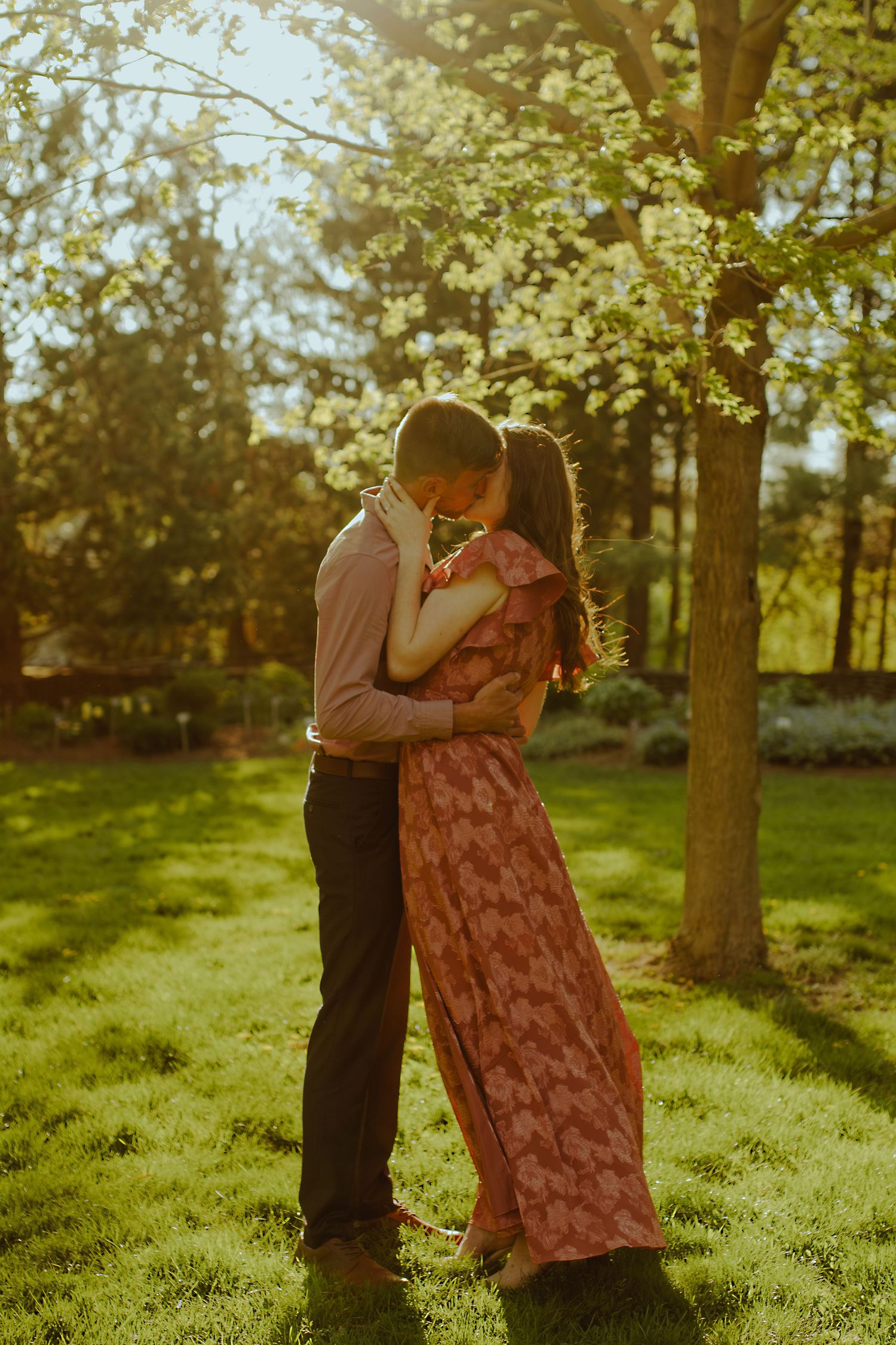 Two figures embrace in a romantic vintage-style scene under trees at sunset with warm golden lighting.