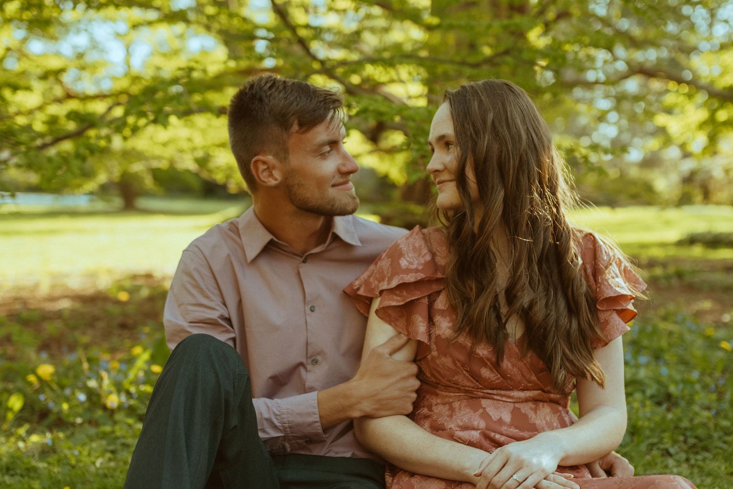 Happy couple shares intimate moment while sitting outdoors in a lush green garden setting.
