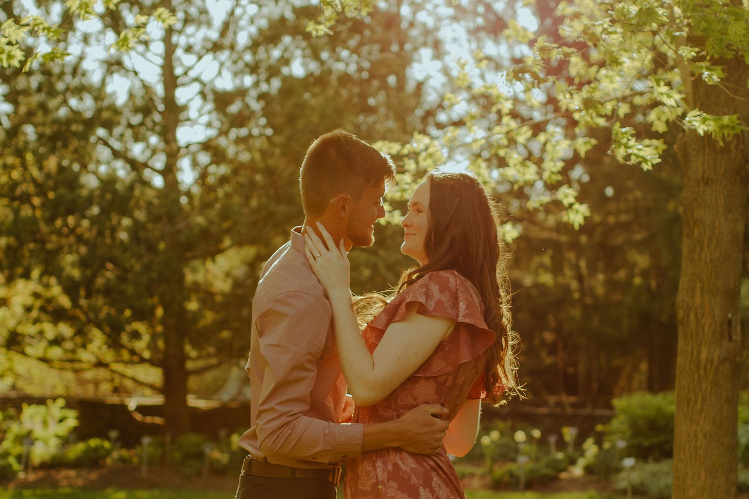 A romantic sunset engagement series featuring a couple embracing among golden sunlit trees in a park.