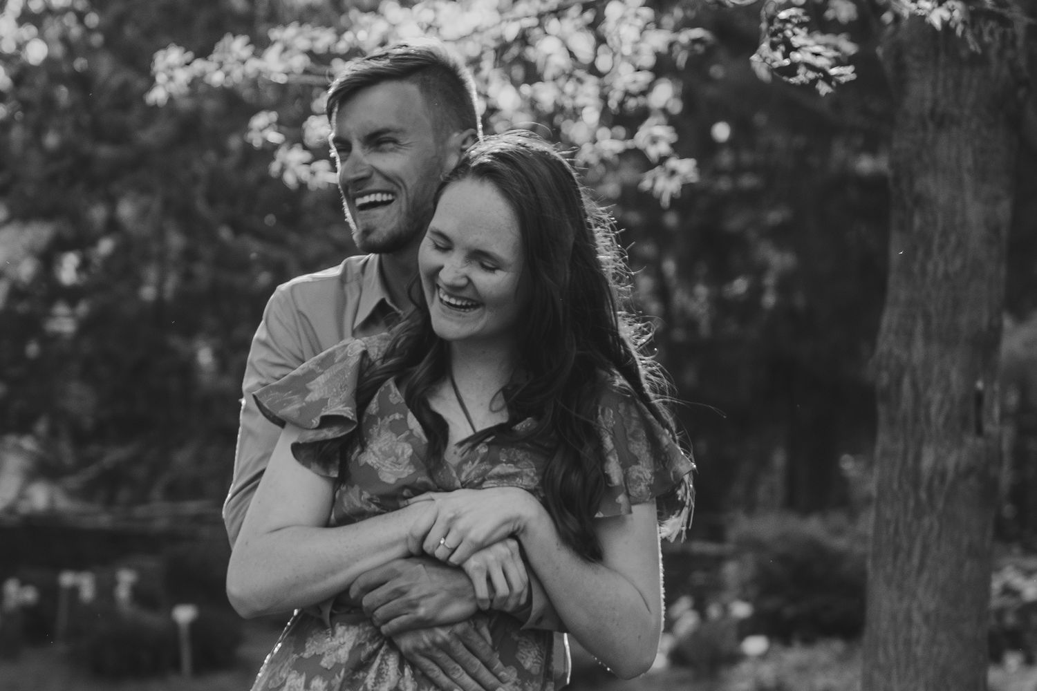 A loving couple shares tender moments during an engagement photo session in a wooded outdoor setting.