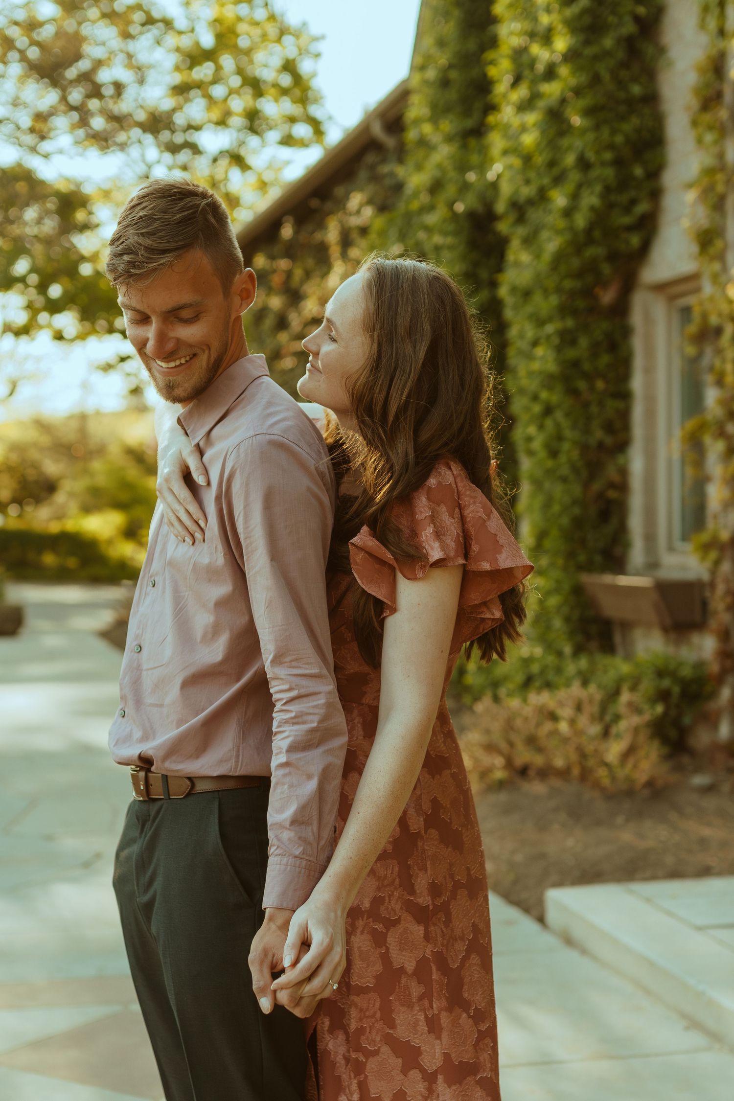 A couple shares an intimate moment while standing together on a sidewalk at sunset.