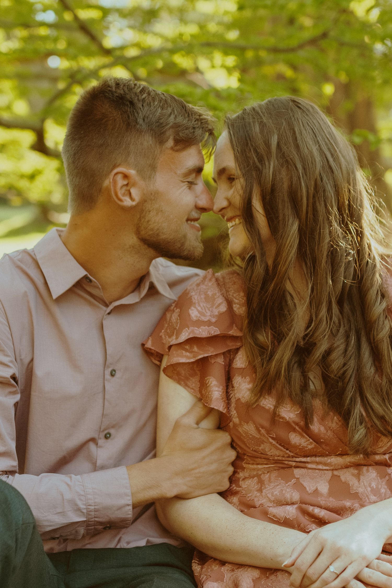 Intimate couple sharing tender moments on a sunny day surrounded by lush green foliage.