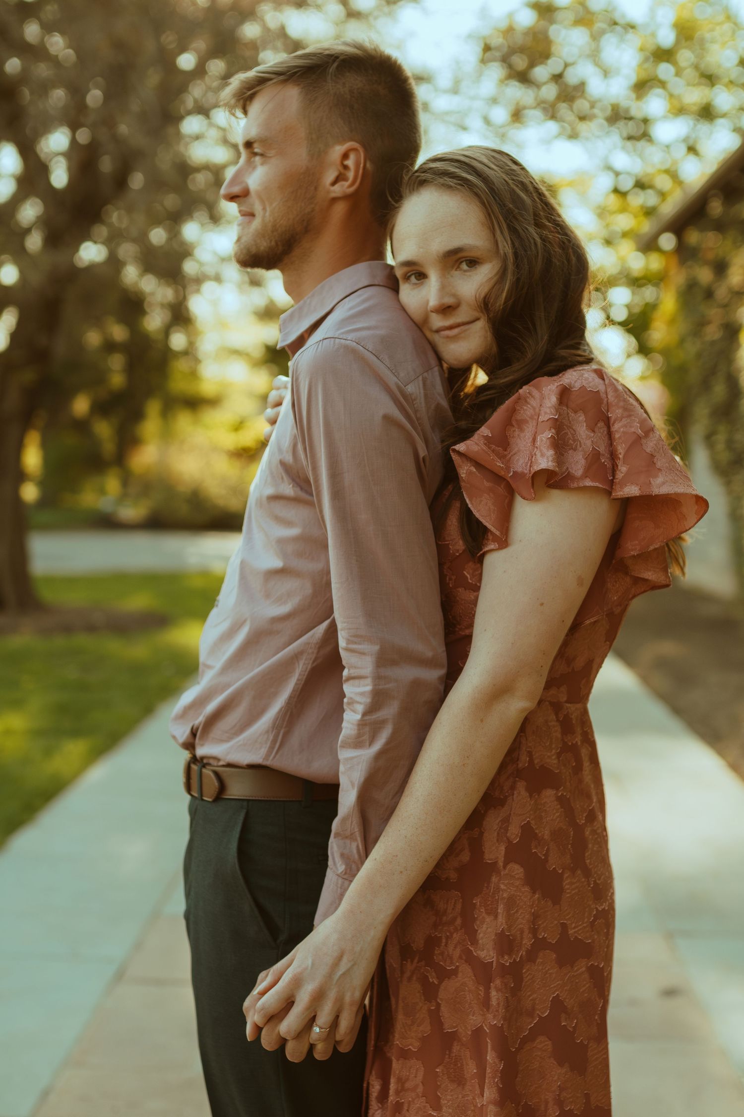 A couple walks together on a sunlit path wearing coordinated formal attire.