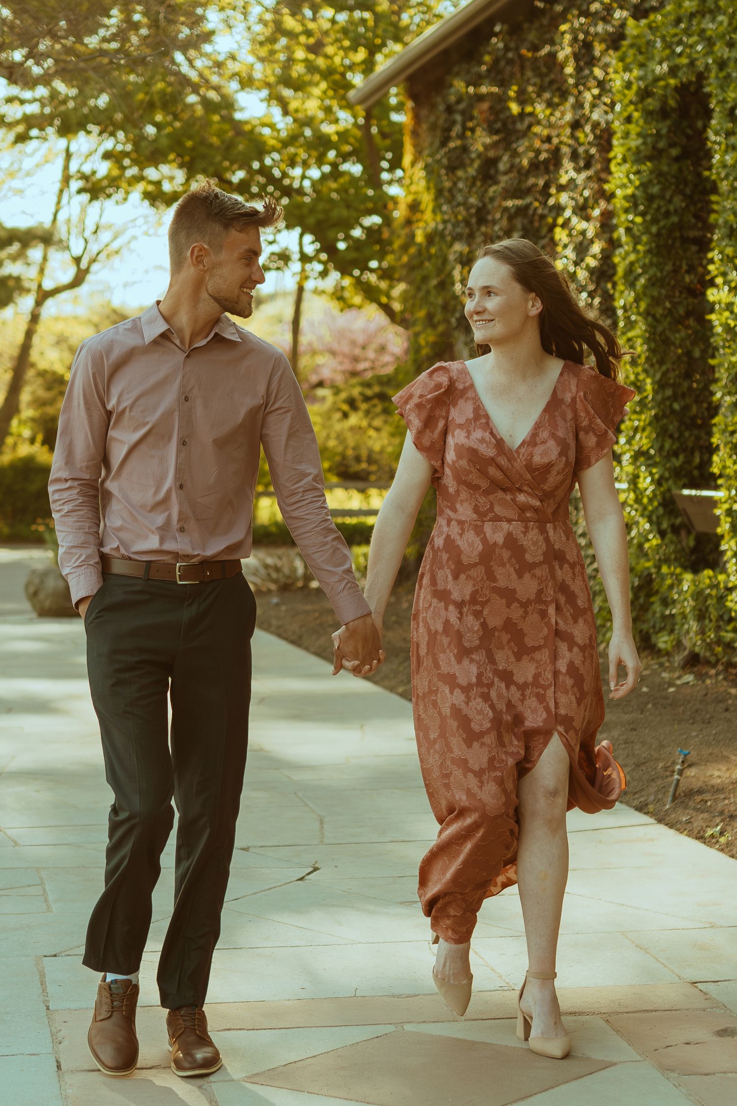 Couple dancing on a paved pathway surrounded by lush greenery and trees.