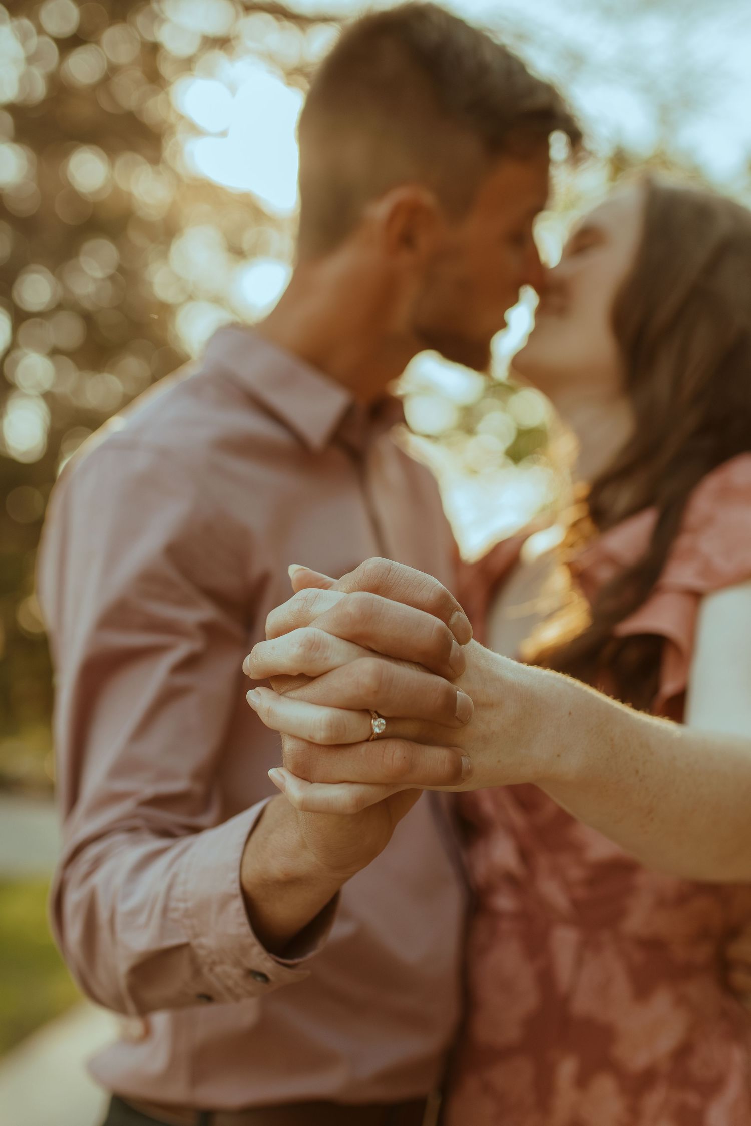 A close-up shot of hands as a couple shares a tender moment in warm sunlight.