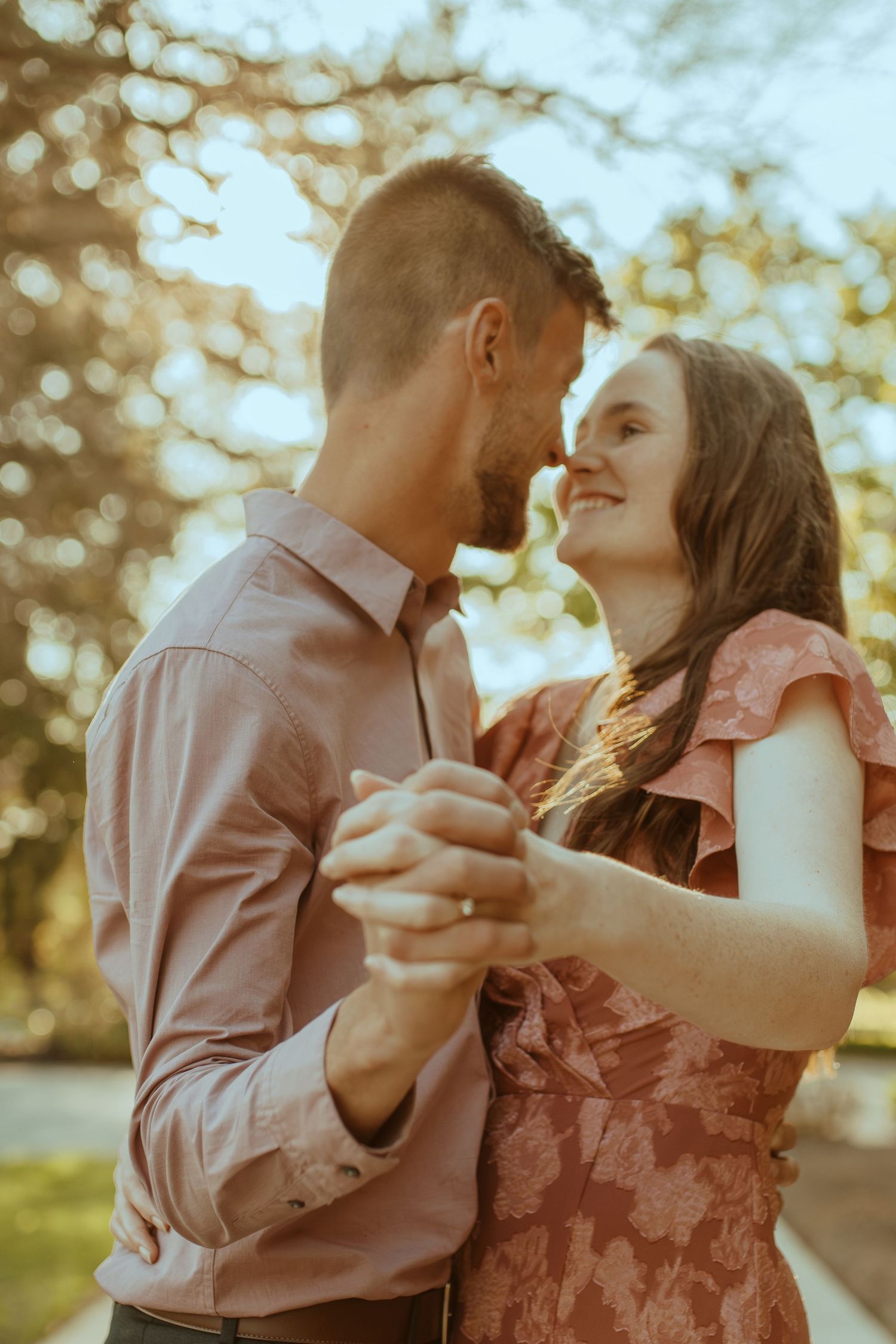 Romantic couple sharing an intimate dance together in warm sunlight with bokeh background effects.