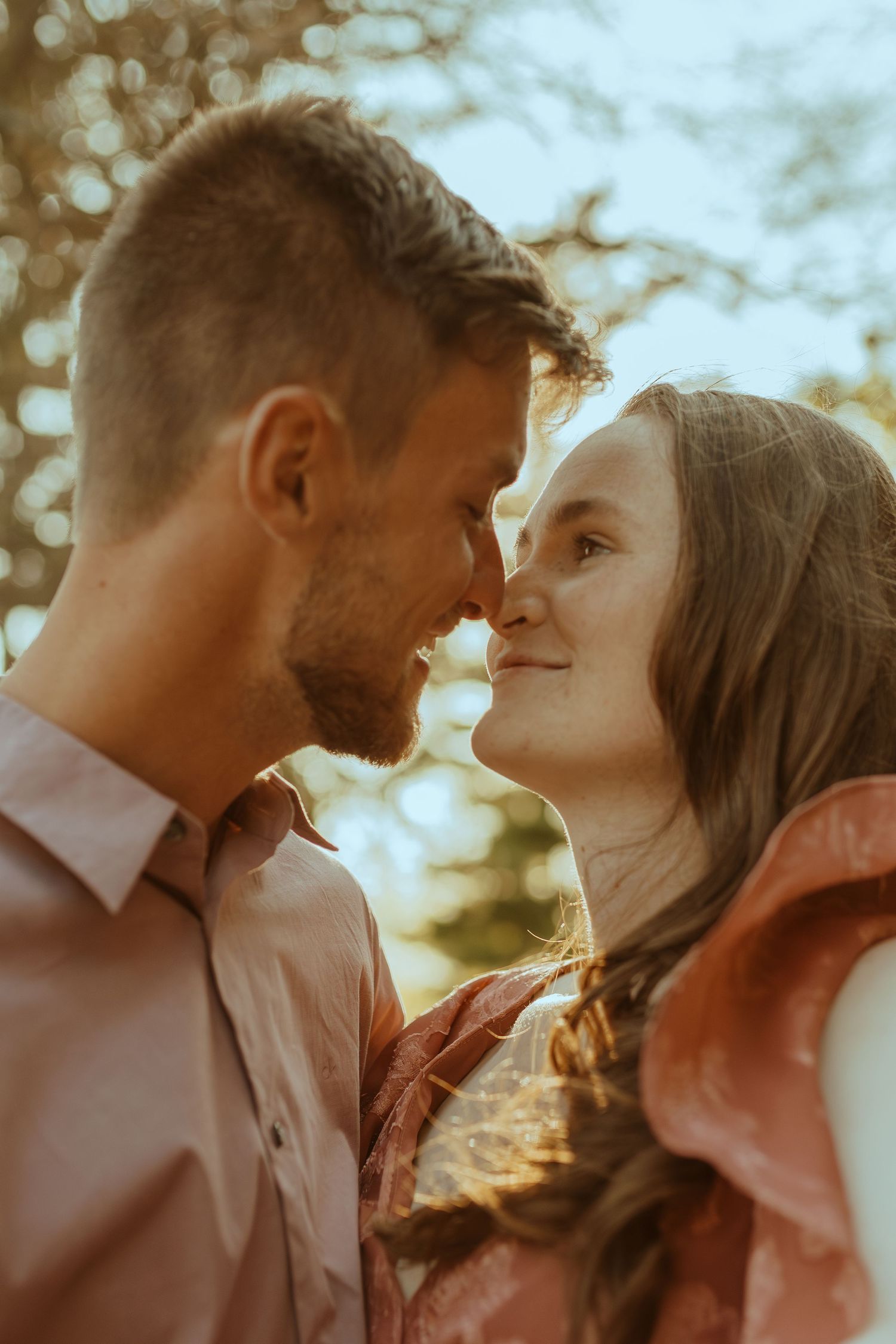 Close-up shot of a couple in tender embrace with soft golden lighting and blurred natural background.