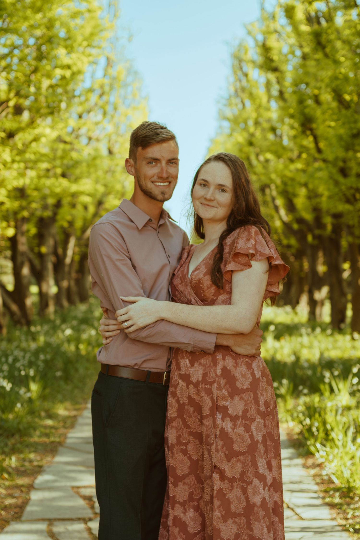 A series of joyful engagement photos captured in a sunny orchard with blooming trees.