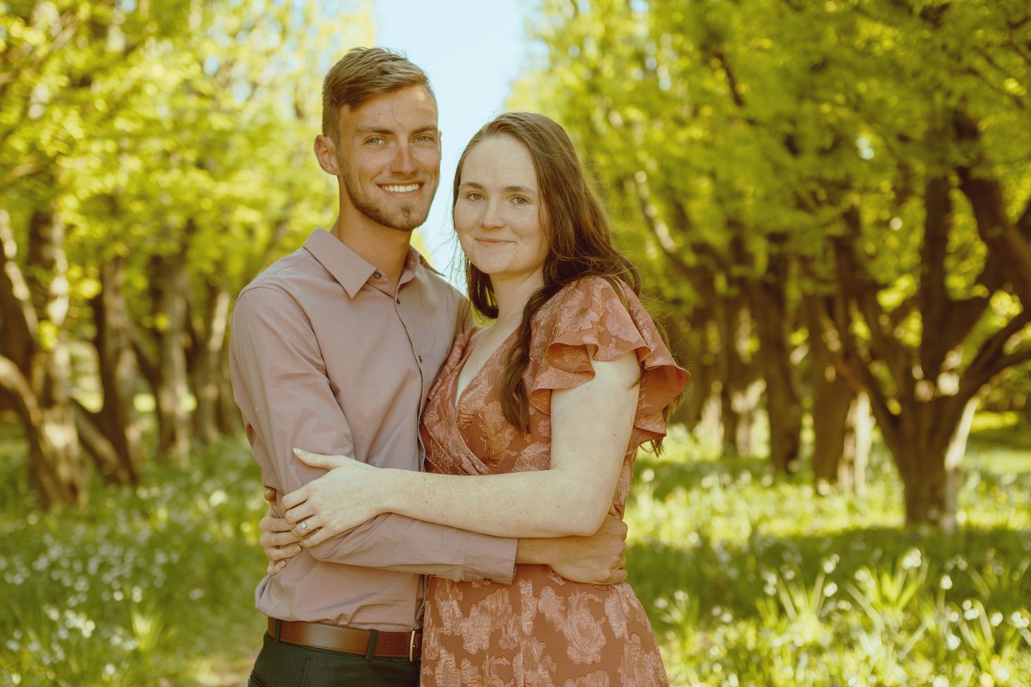 A couple shares tender moments together in a sunlit outdoor garden pathway.