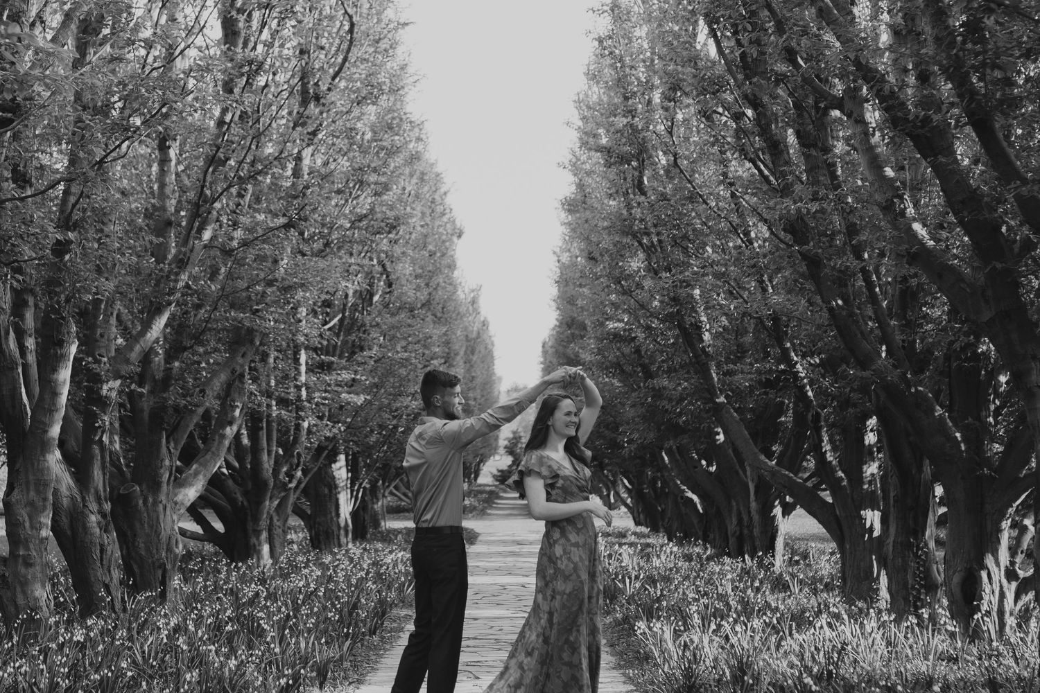 Tree-lined path with couples enjoying romantic moments in black and white photography.