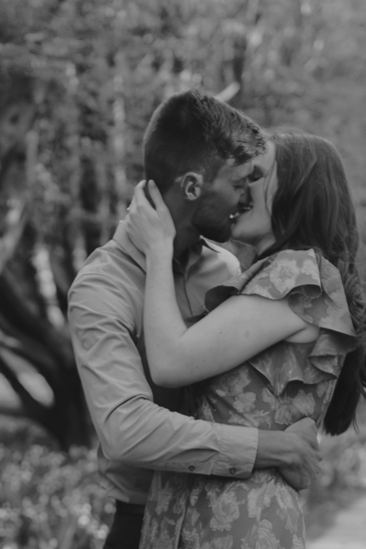 A black and white photo captures an intimate embrace between a couple outdoors.