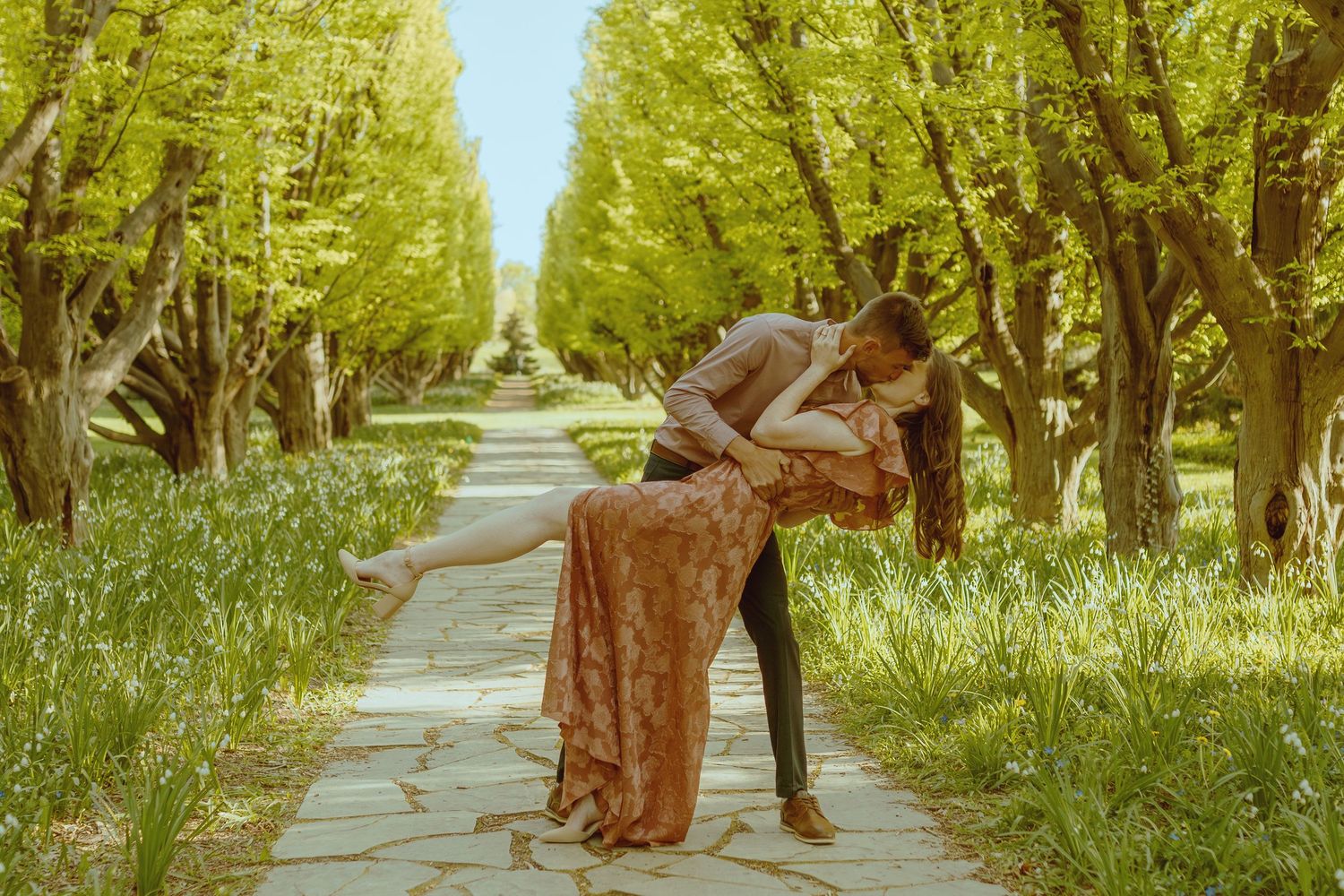 Tree-lined pathway with couple walking together in soft golden sunlight.