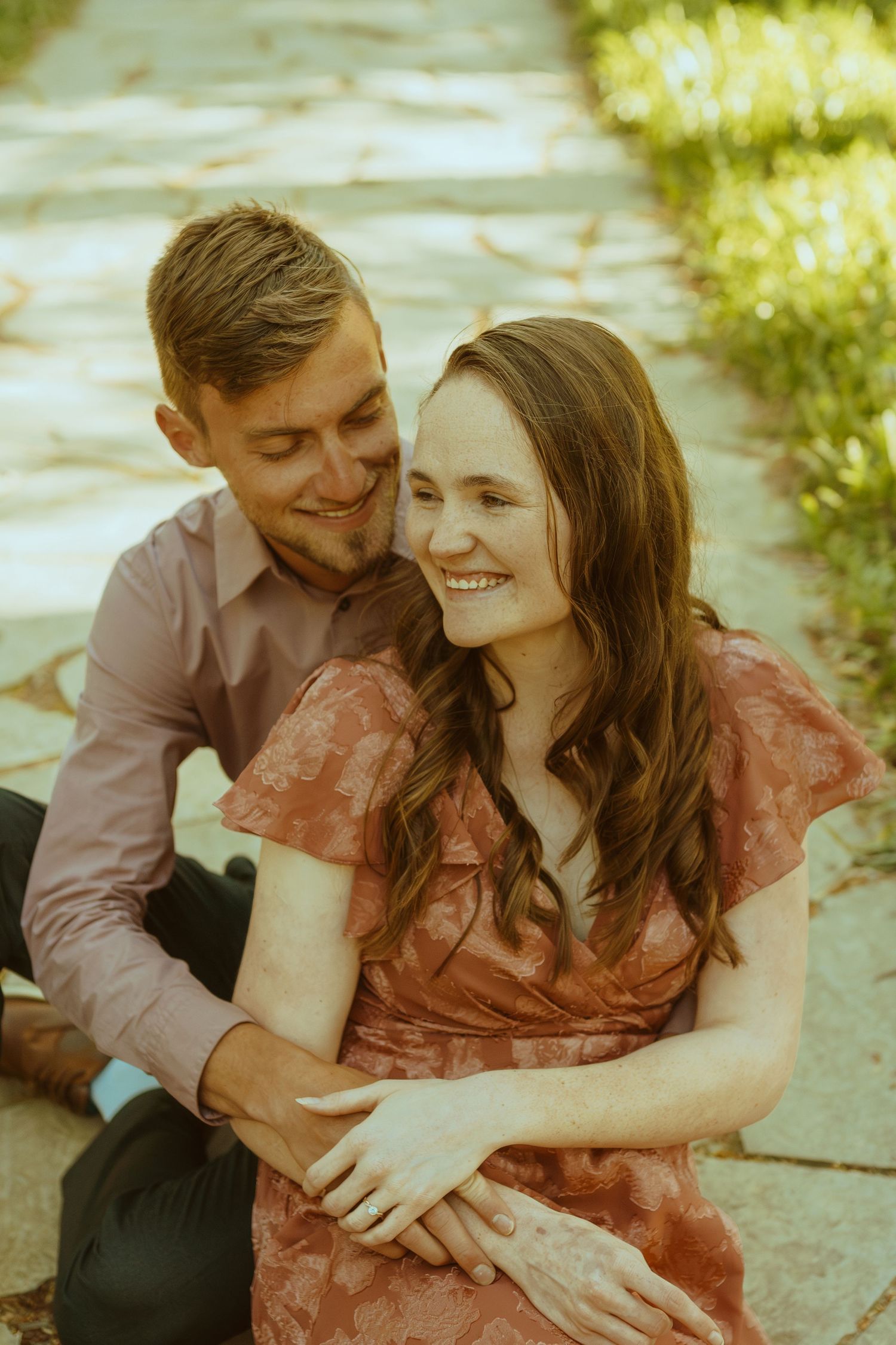 A couple shares loving moments while sitting together outdoors in golden sunlight.