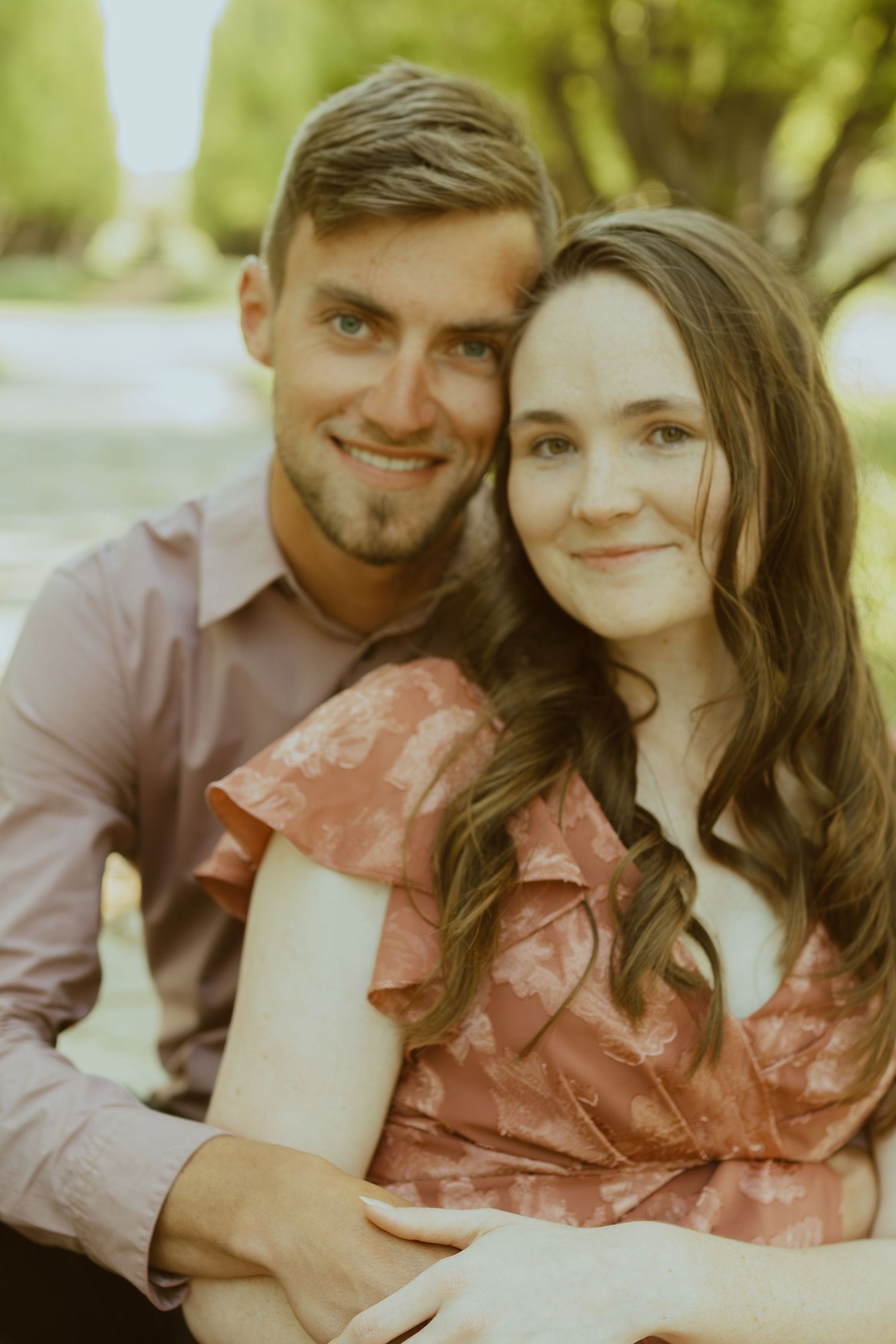Couple embracing in soft natural lighting with trees in background.