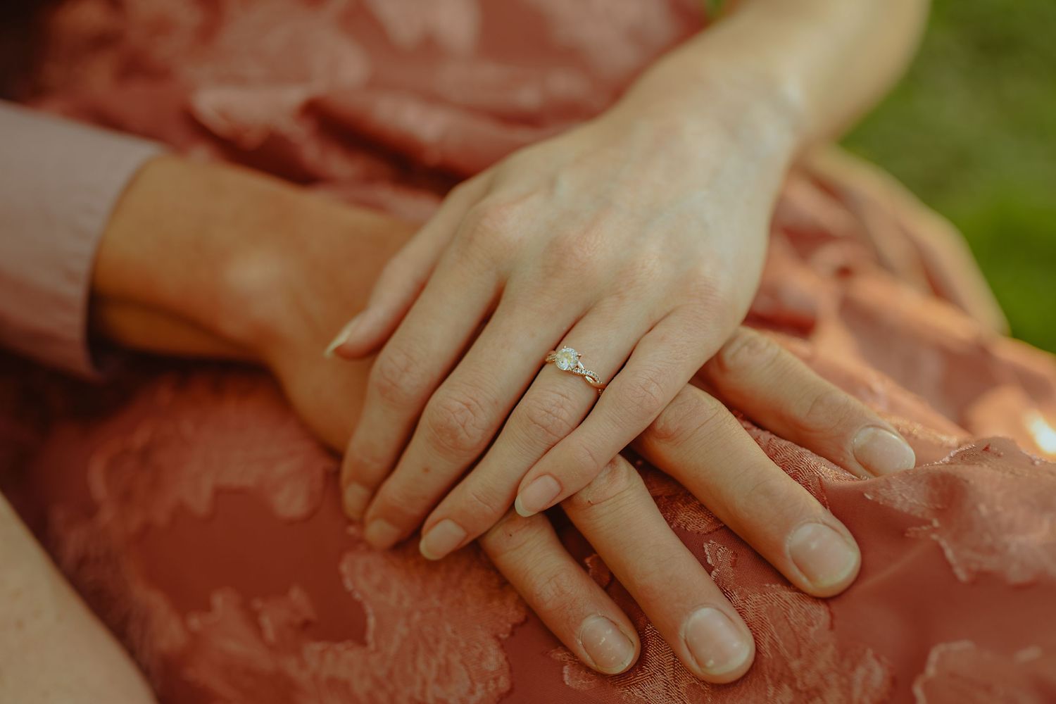Close-up of hands wearing wedding rings resting on coral-colored fabric.