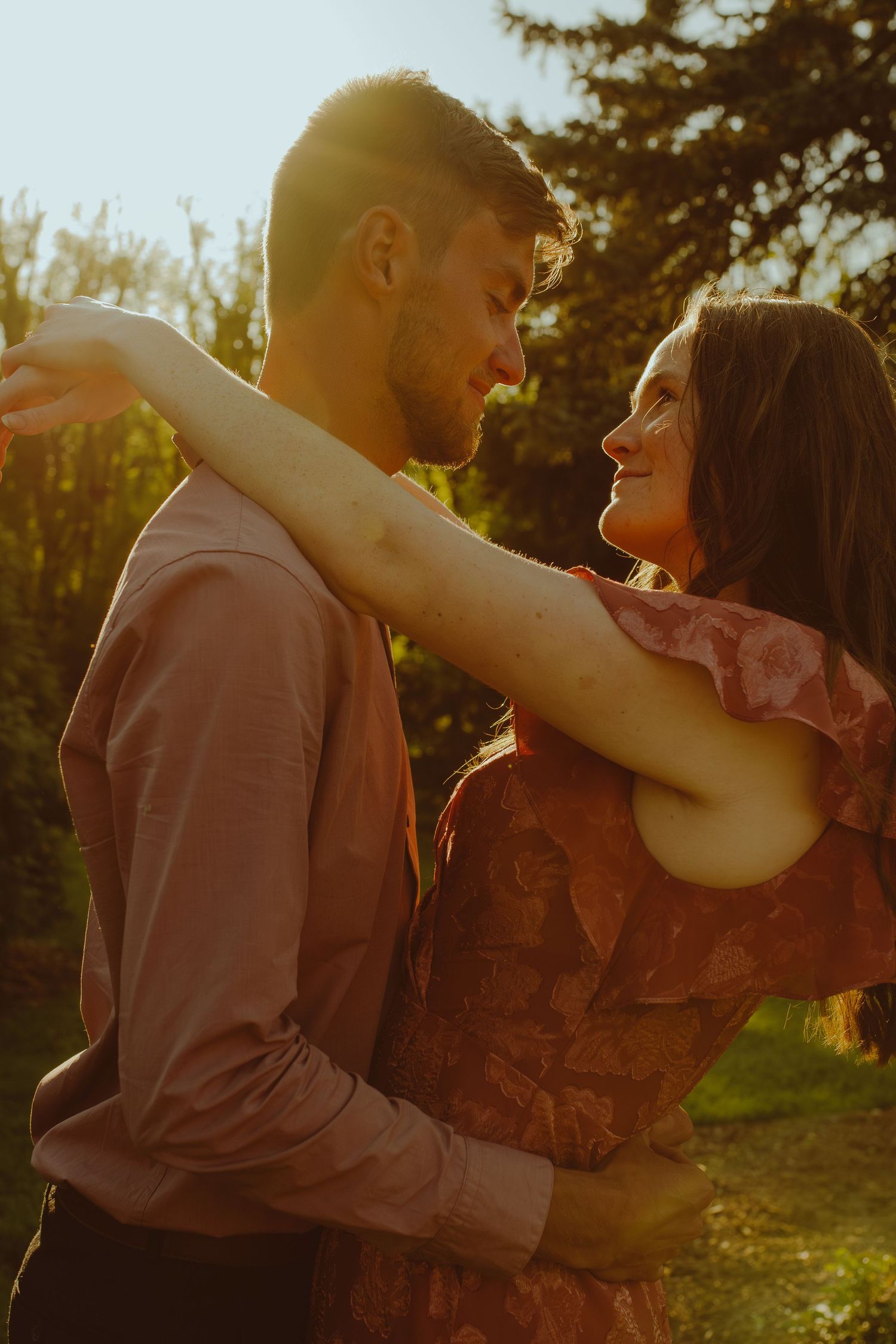 A couple dancing in sunlit forest while wearing vintage-inspired clothing in warm sunset lighting.
