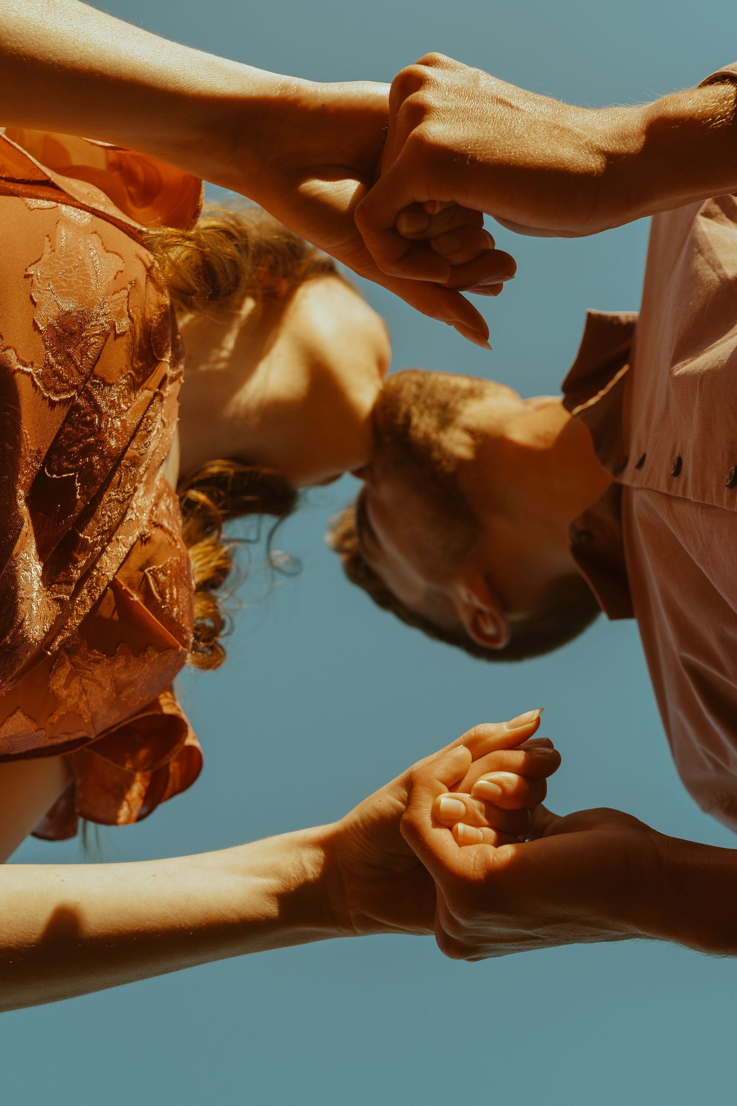 Multiple hands reach out against a blue sky in a warm tinted photograph showing connection and unity.