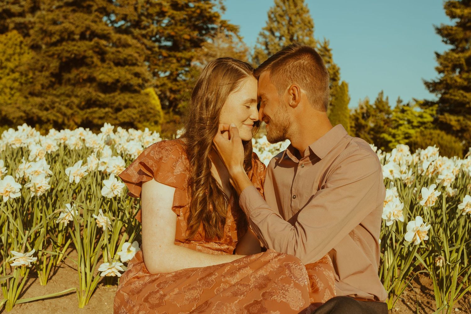 Intimate couple sharing a romantic moment in a field of blooming white daffodils during golden hour.