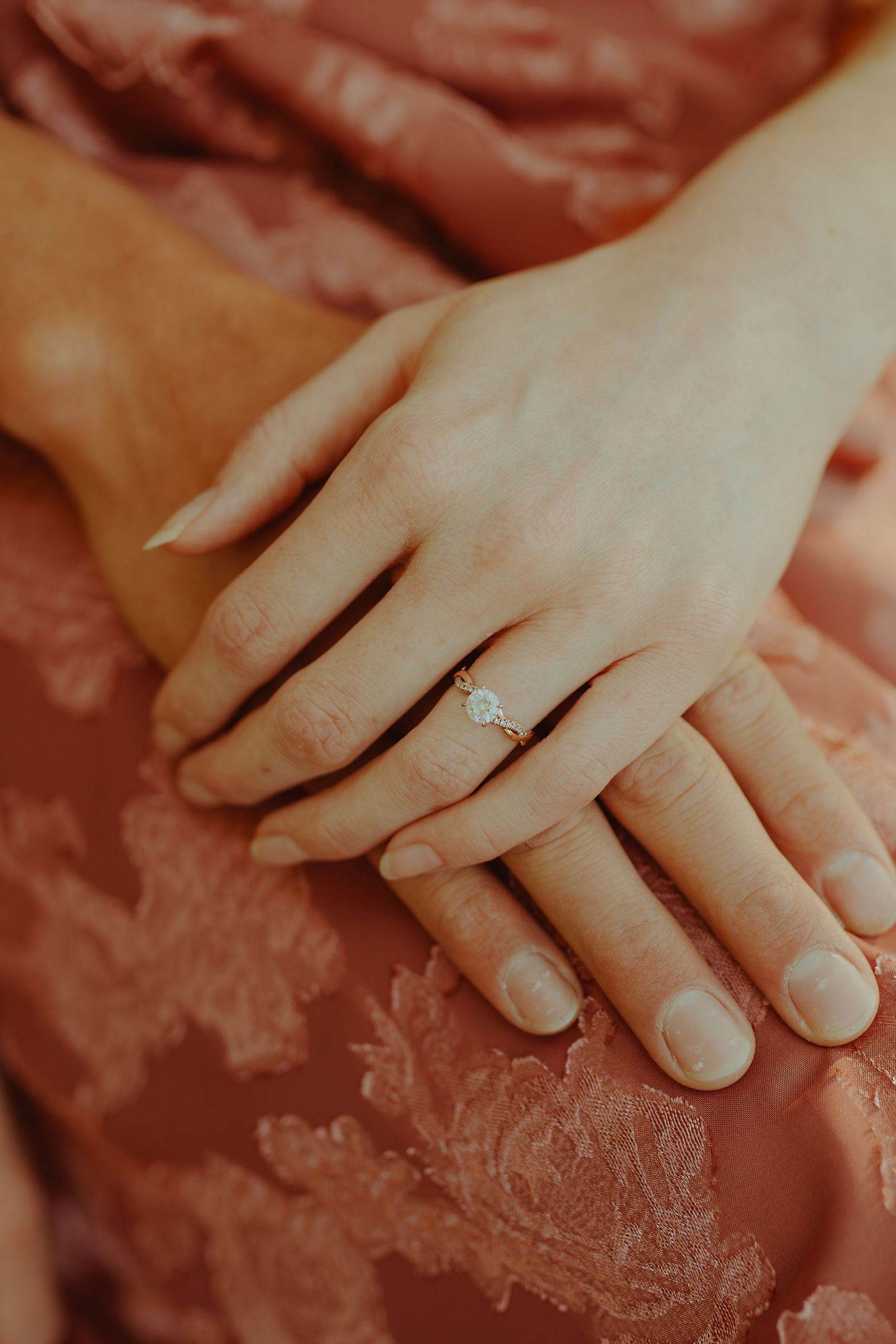Close-up view of hands with an engagement ring resting on pink floral fabric.