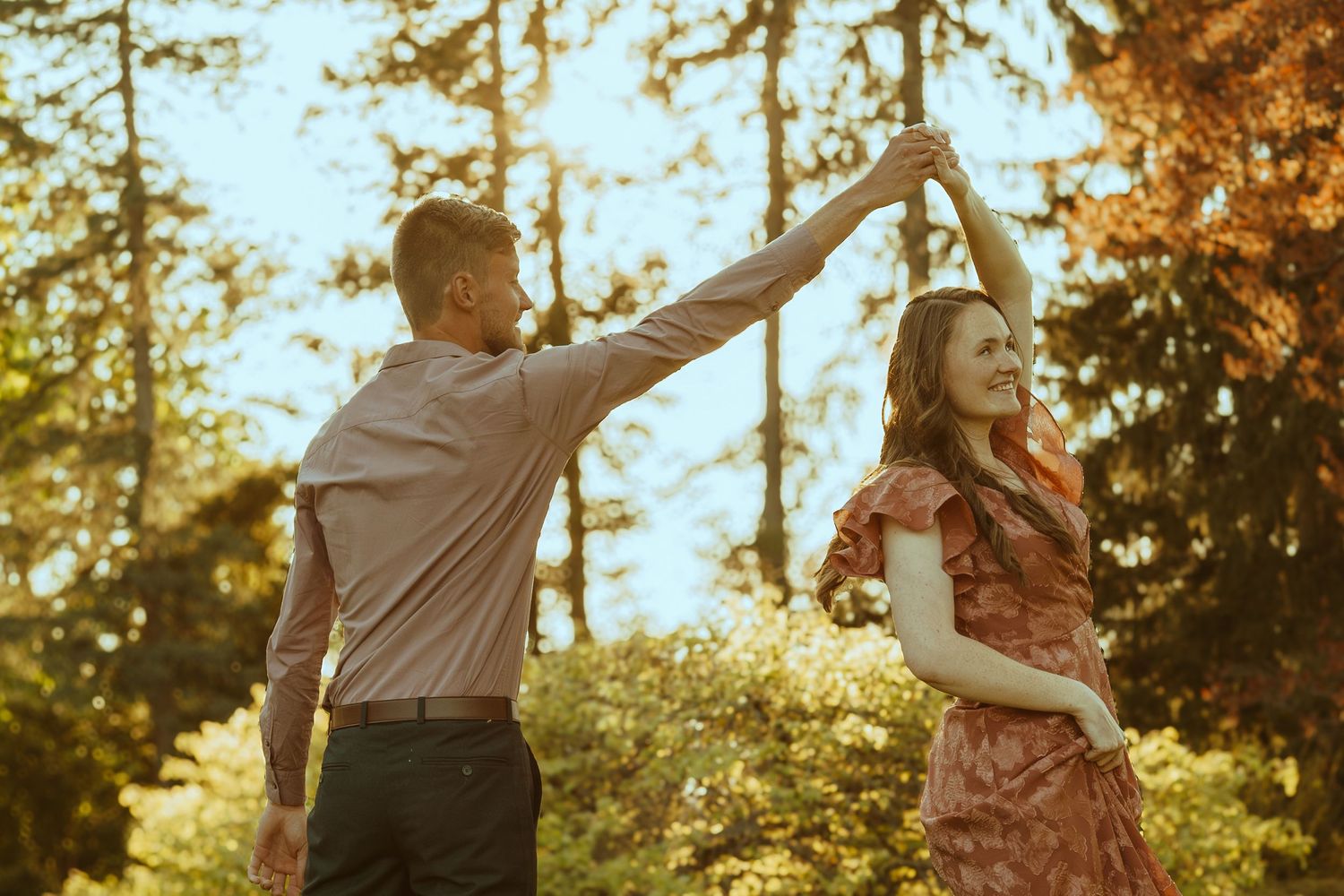 Young people enjoying a sunset dance celebration in a scenic outdoor park with golden sunlight filtering through trees.