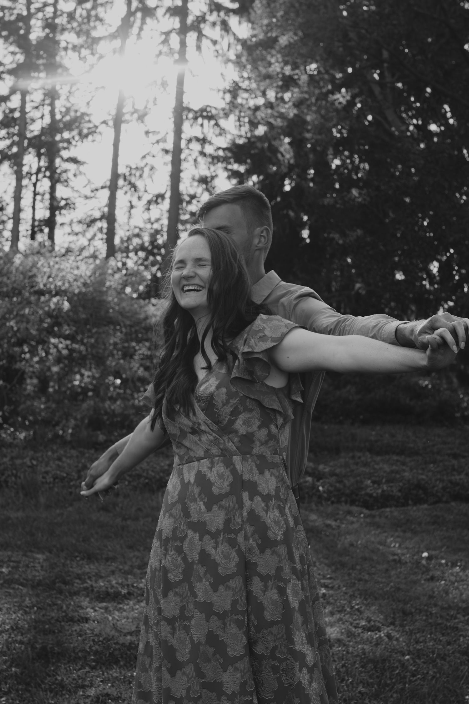 Person in a patterned dress twirls joyfully in a wooded outdoor setting captured in black and white.