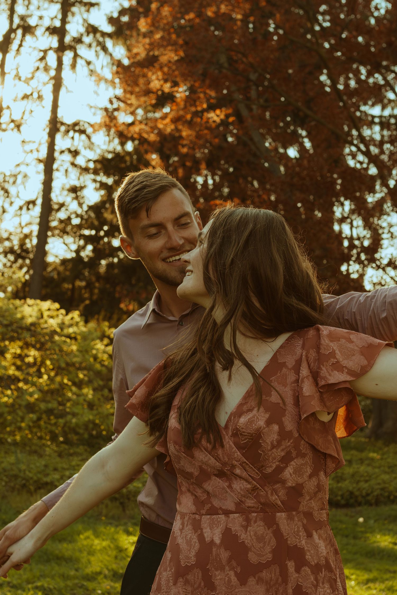 Dancing couple enjoy a romantic moment outdoors with sunlit trees in the background.