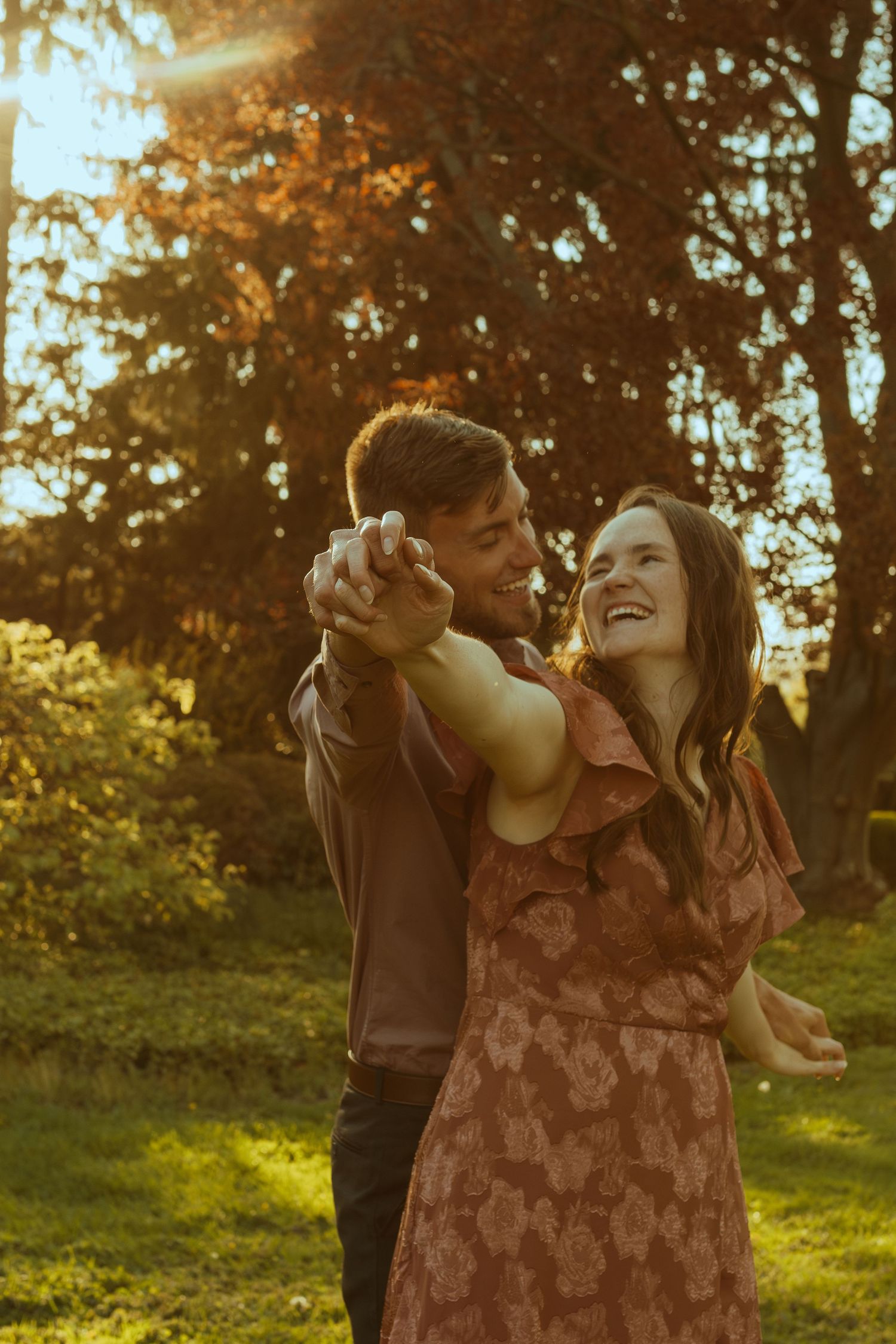 A romantic couple embraces in a sunlit outdoor setting with golden hour lighting and trees in the background.