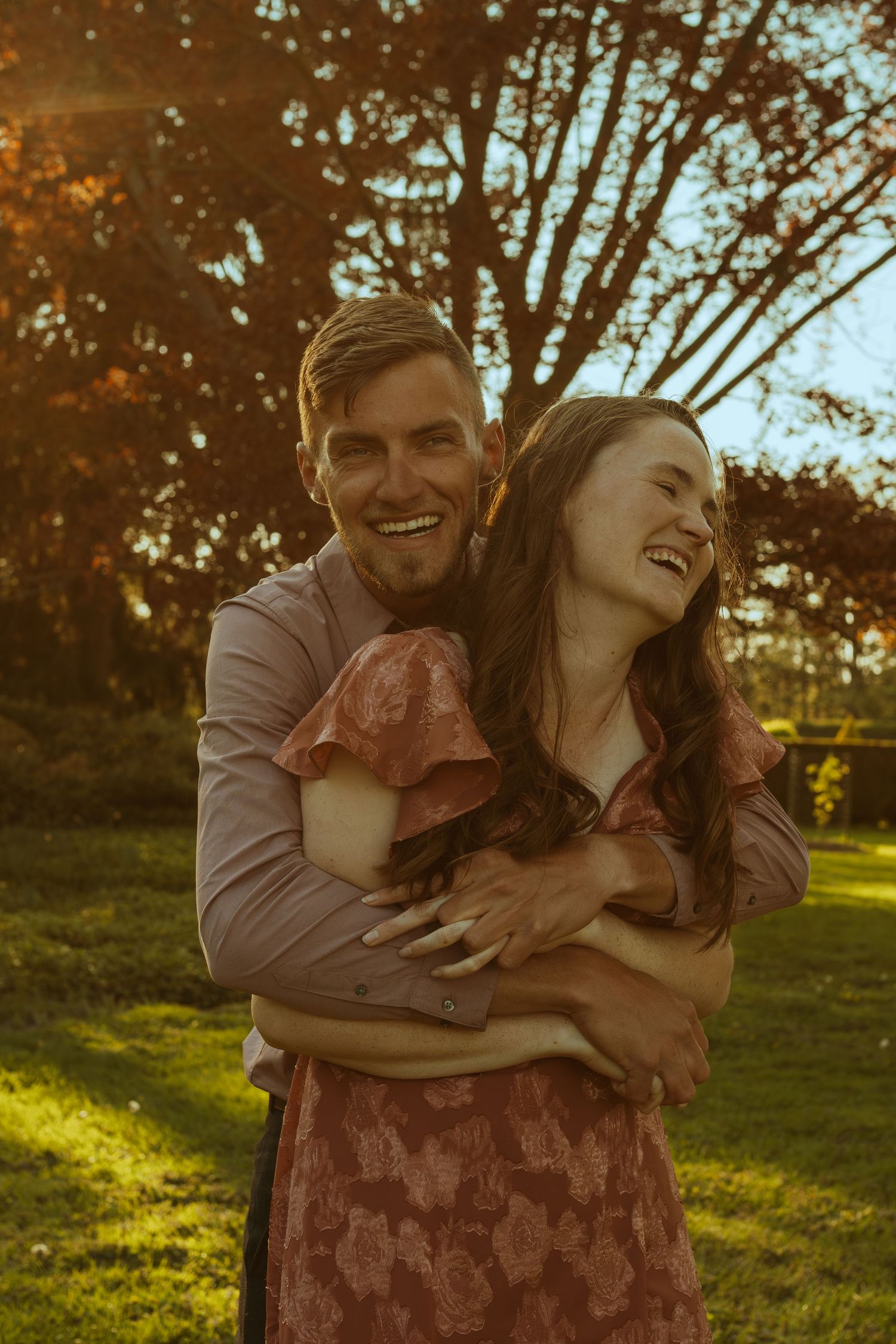 A joyful couple laughs while sharing an intimate moment outdoors at sunset.