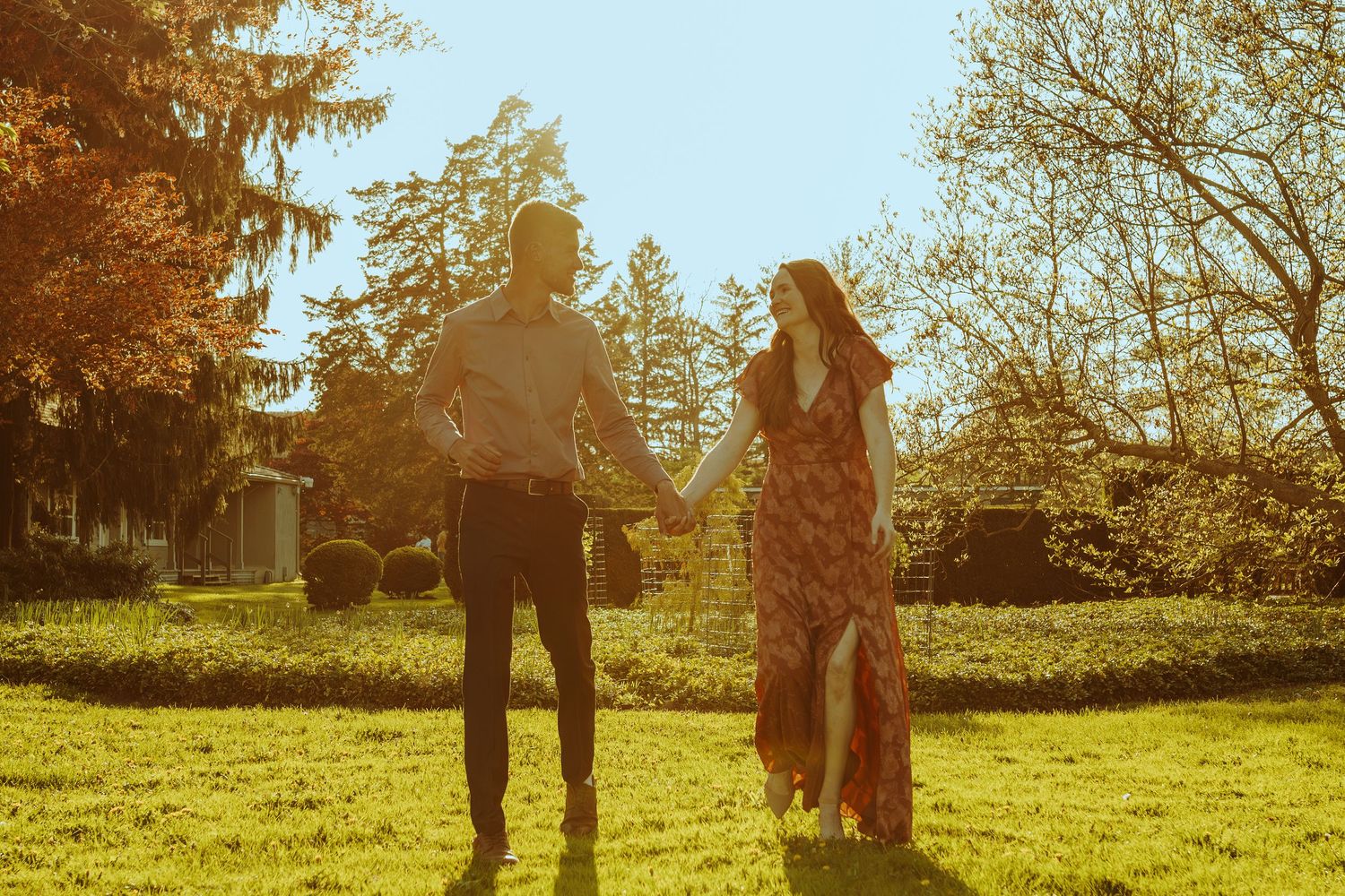 Silhouetted couple stands together in a sunny autumn park with golden leaves and trees in the background.