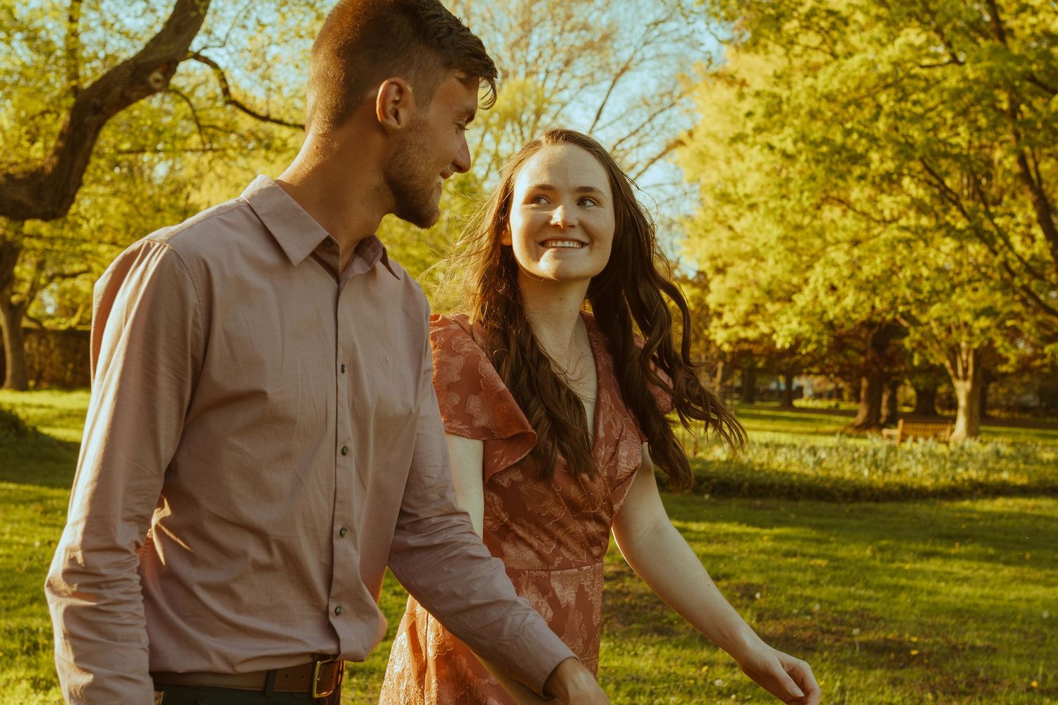 A couple shares a romantic moment together while walking through a sunlit autumn park with golden leaves.