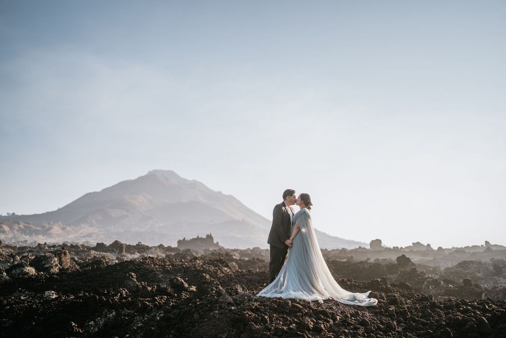 Two people in formal attire embrace on a rocky mountain landscape.