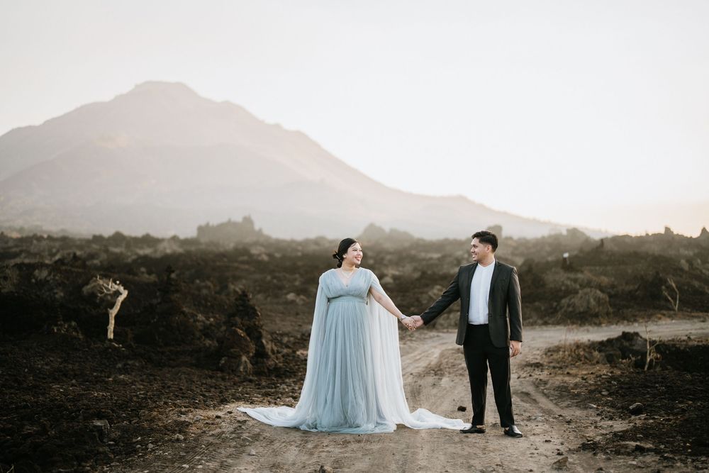 Two people in formal wear stand together on volcanic terrain at sunset.