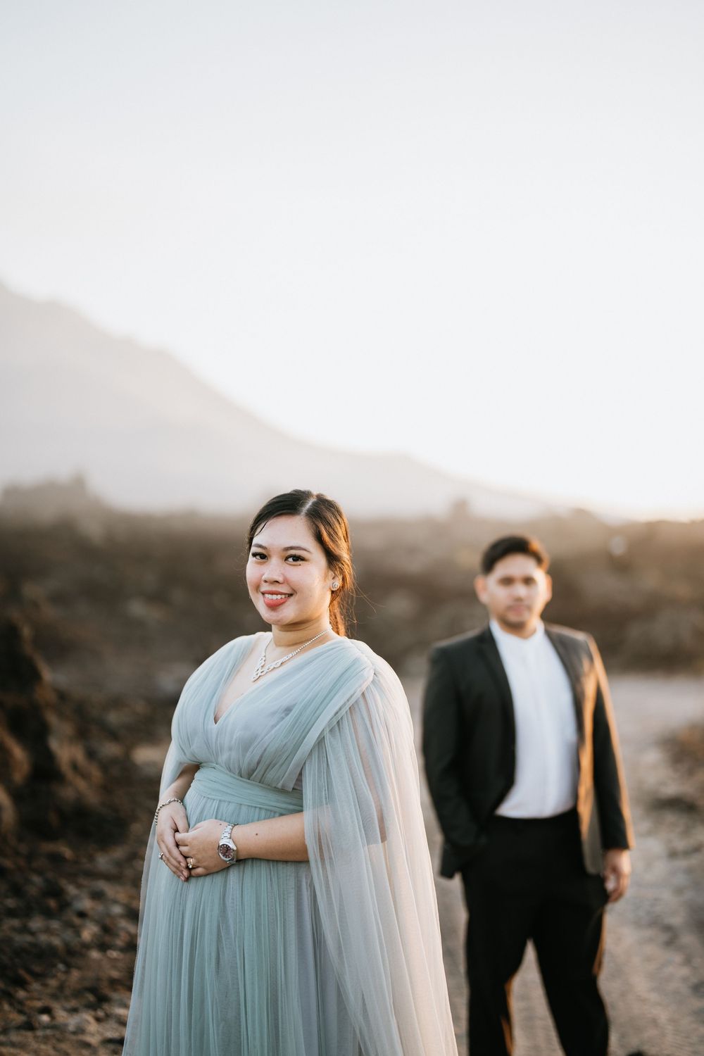 A couple in formal wear poses on rocky terrain during golden hour.