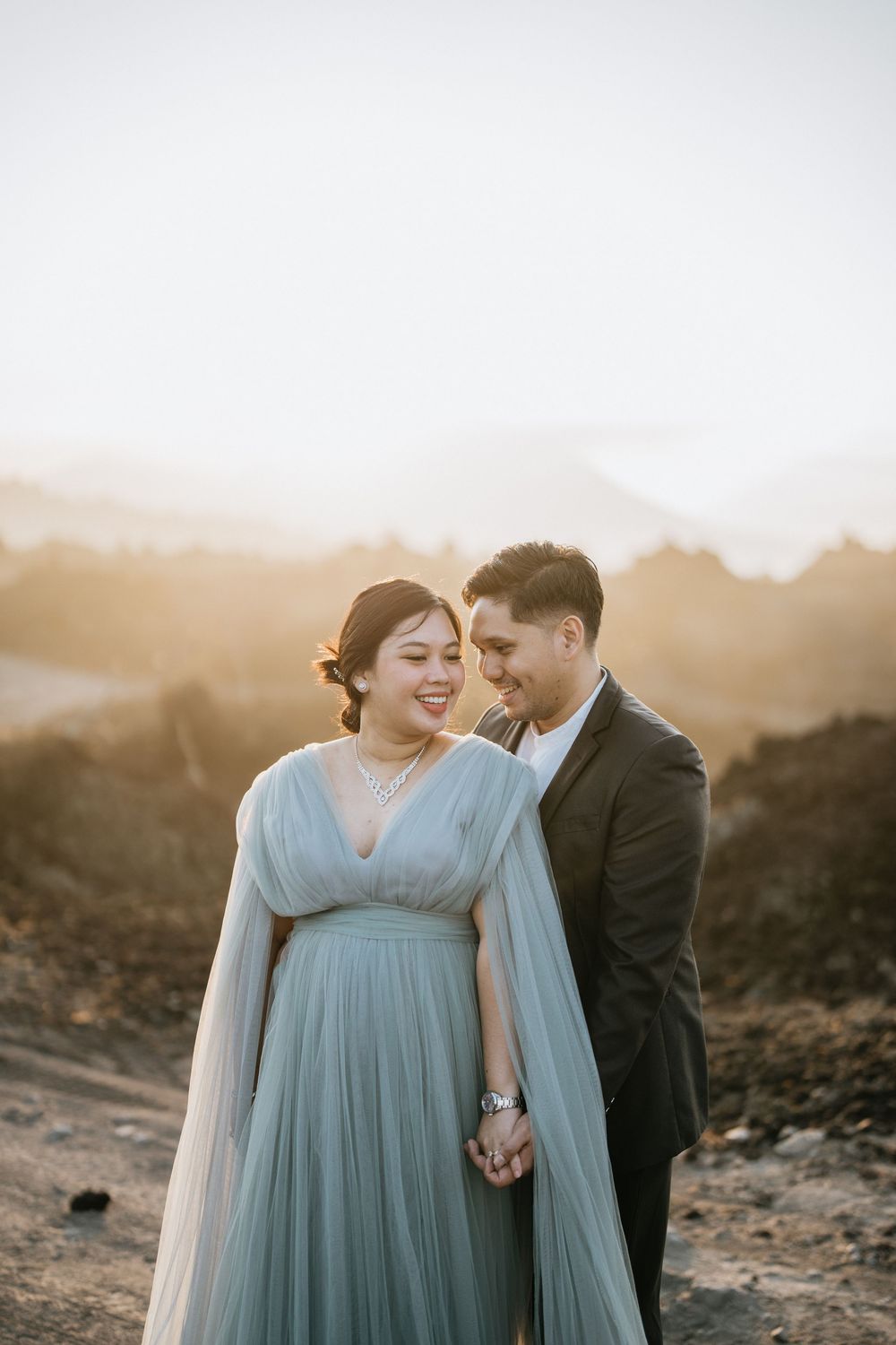 A romantic moment captured between a couple wearing blue dress and black suit against a mountain backdrop.