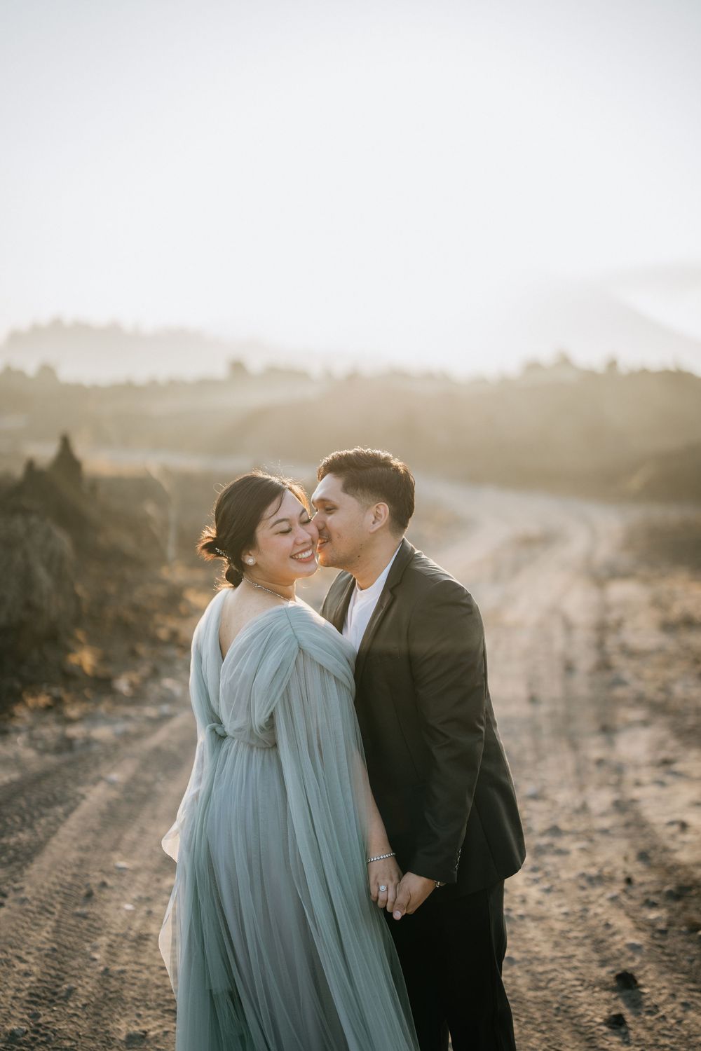 A tender moment between a couple in formal wear against a mountainous landscape at sunset.
