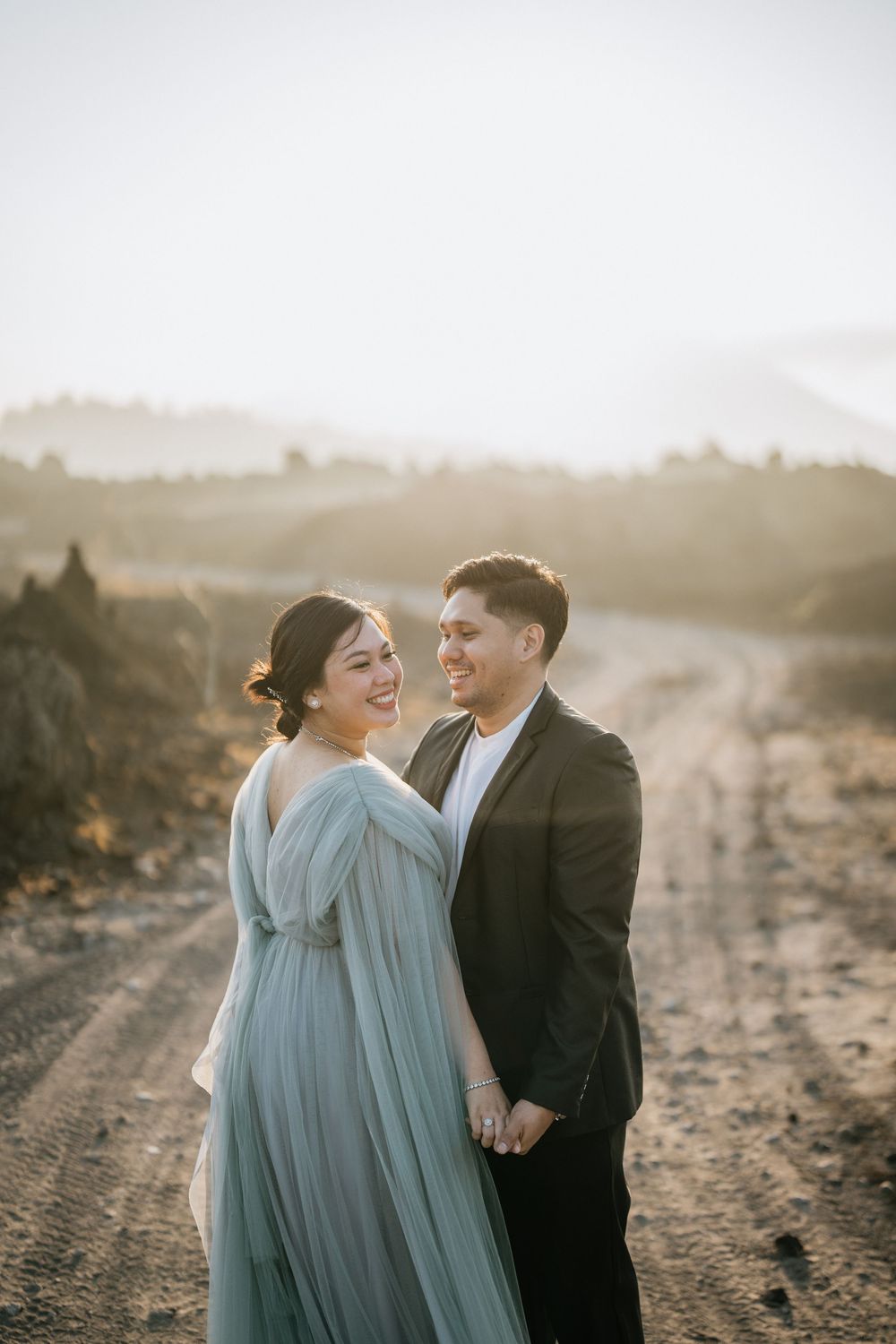 A joyful couple shares a laugh while wearing formal attire in a mountainous setting.