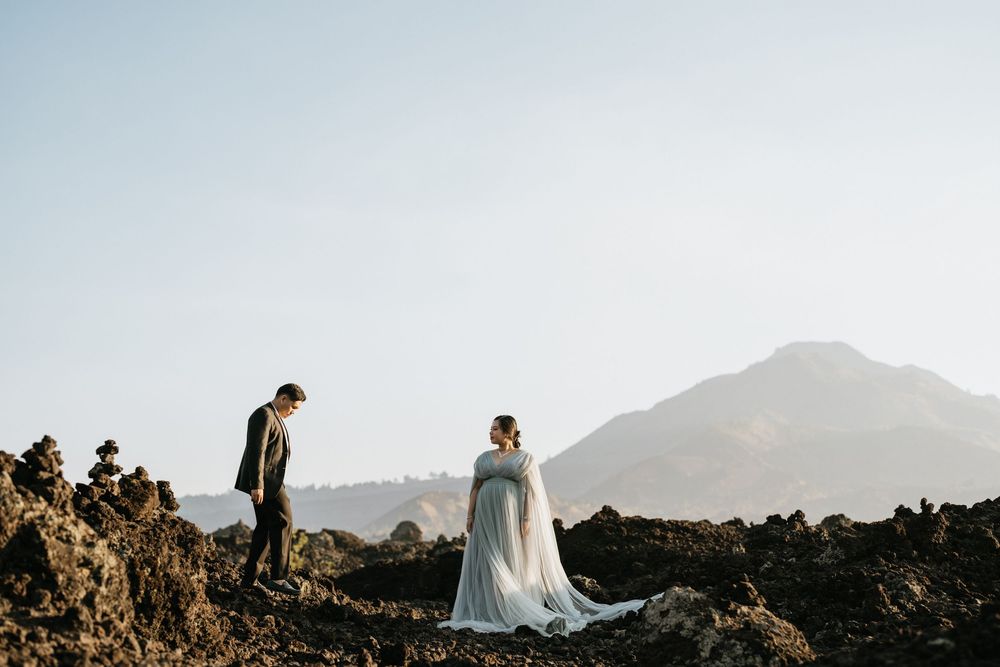A romantic photoshoot featuring a couple on rocky terrain with mountains in the background.