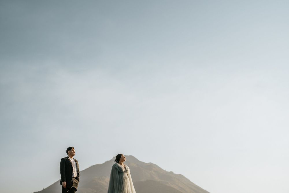 Wedding couple stands silhouetted against misty mountain peaks and sky.