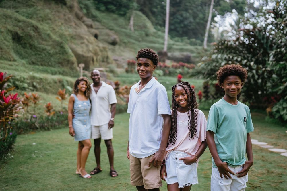 Family walking together on grassy path with palm trees in background.