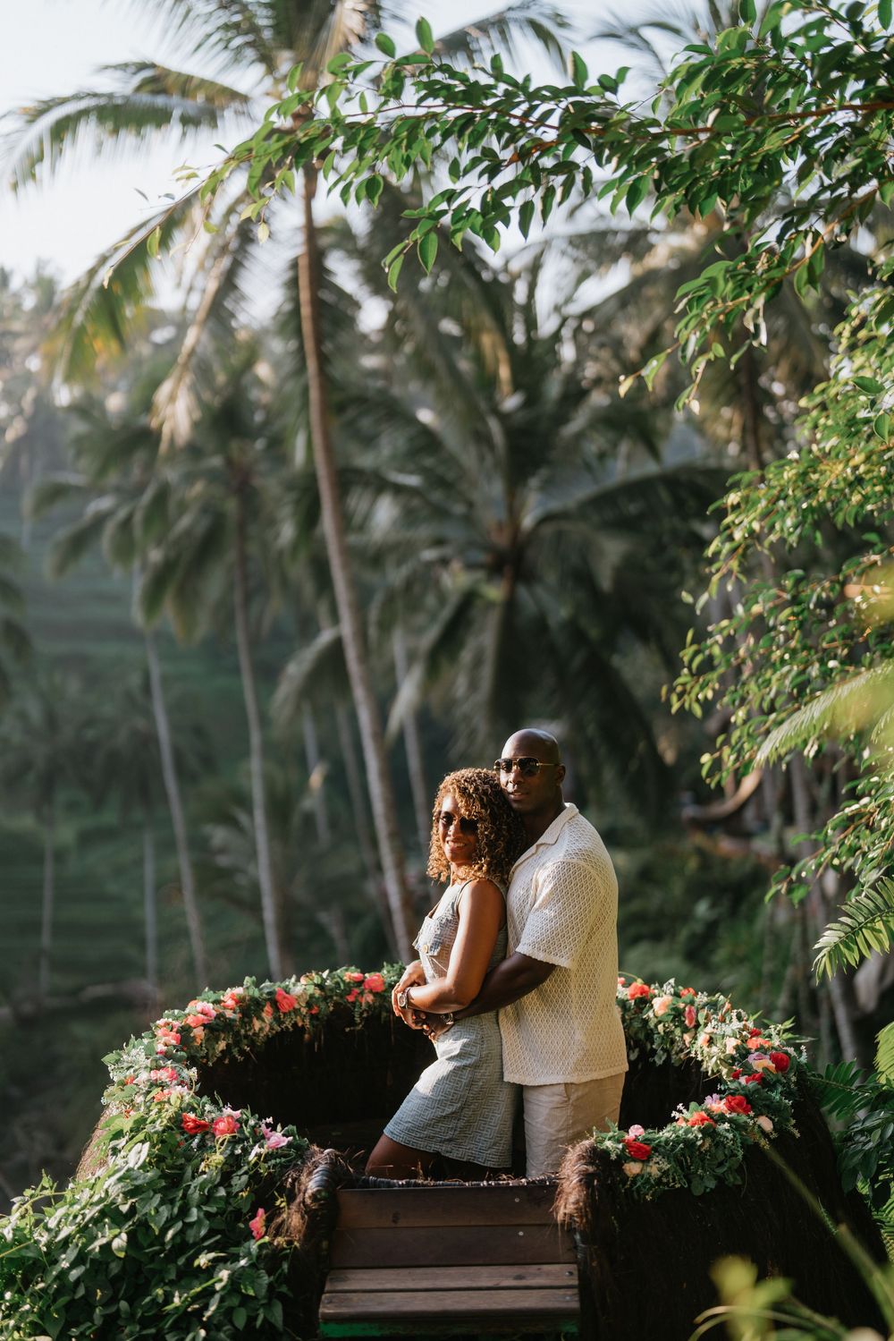 A romantic moment captured on a wooden platform surrounded by tropical palm trees and floral decorations.