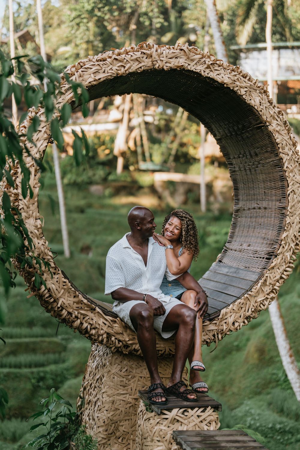 A couple shares a tender moment in a large woven nest swing amidst tropical greenery.