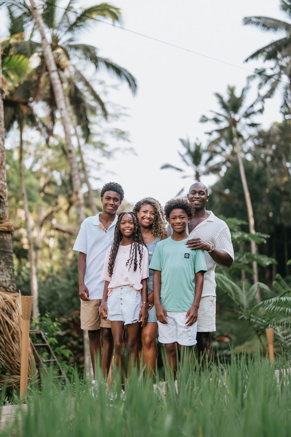 A family portrait taken in a tropical setting with palm trees and lush greenery.