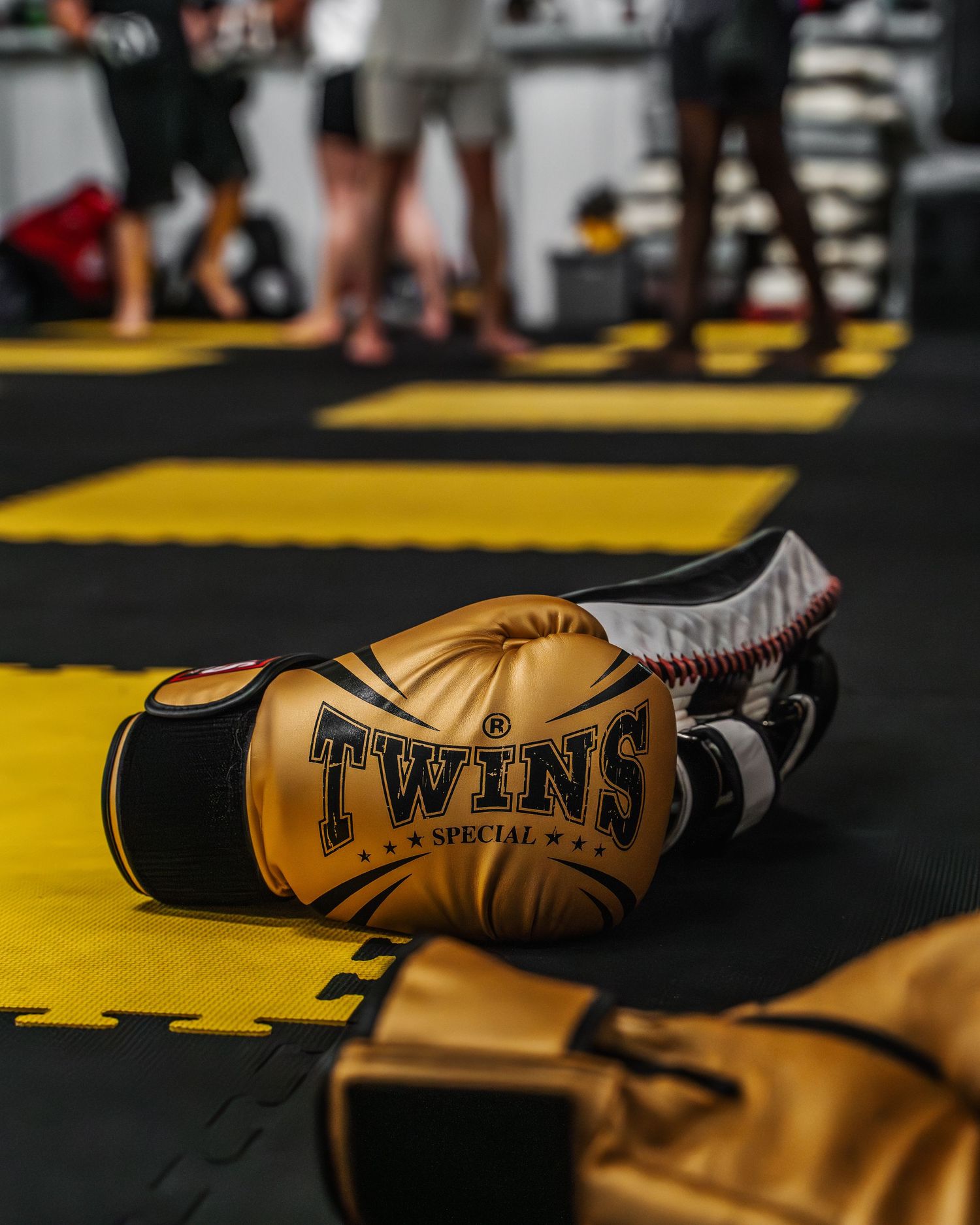 Twins brand boxing gloves in tan leather lying on yellow mat surface.