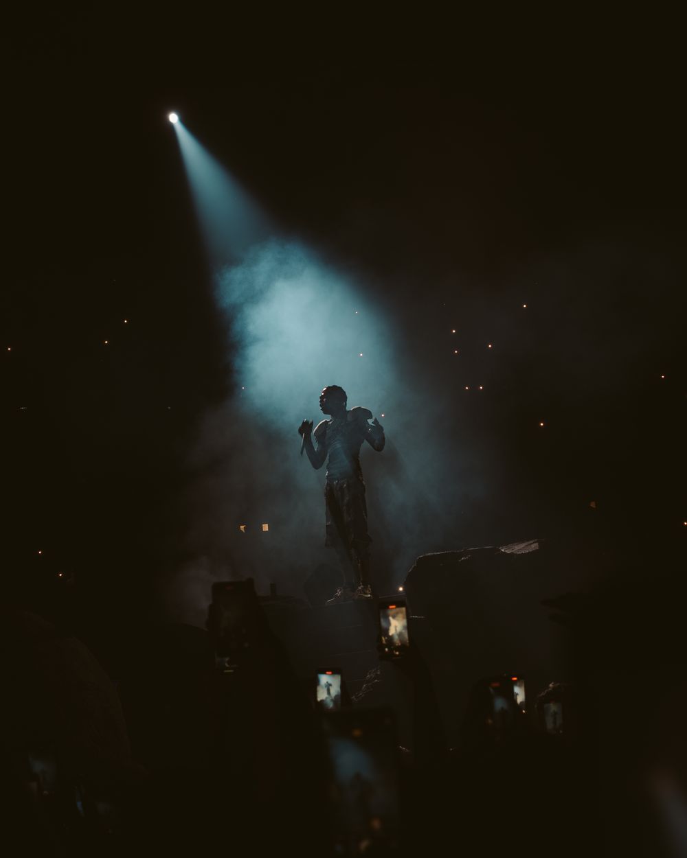 Silhouetted figures perform on a dark stage with atmospheric smoke and dramatic lighting effects.