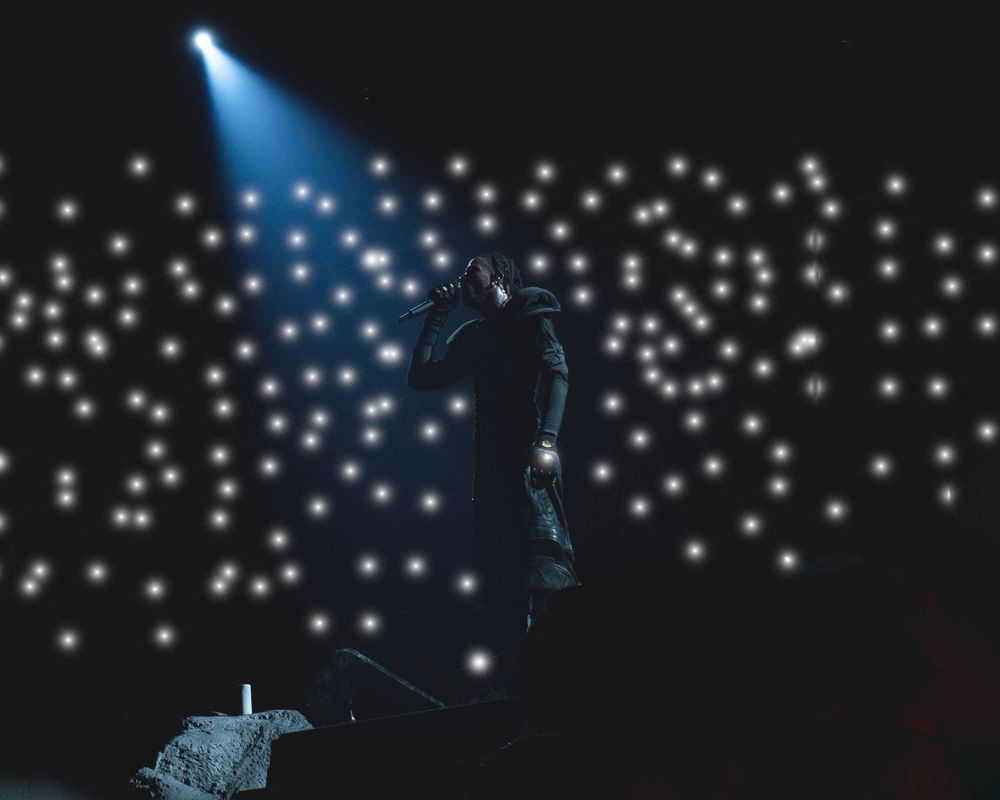 Silhouette of a performer on stage against a backdrop of twinkling star-like lights creating a magical atmosphere.