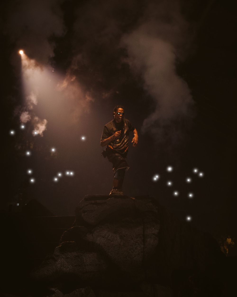 Silhouetted performer stands on elevated platform with dramatic backlighting and smoke effects.